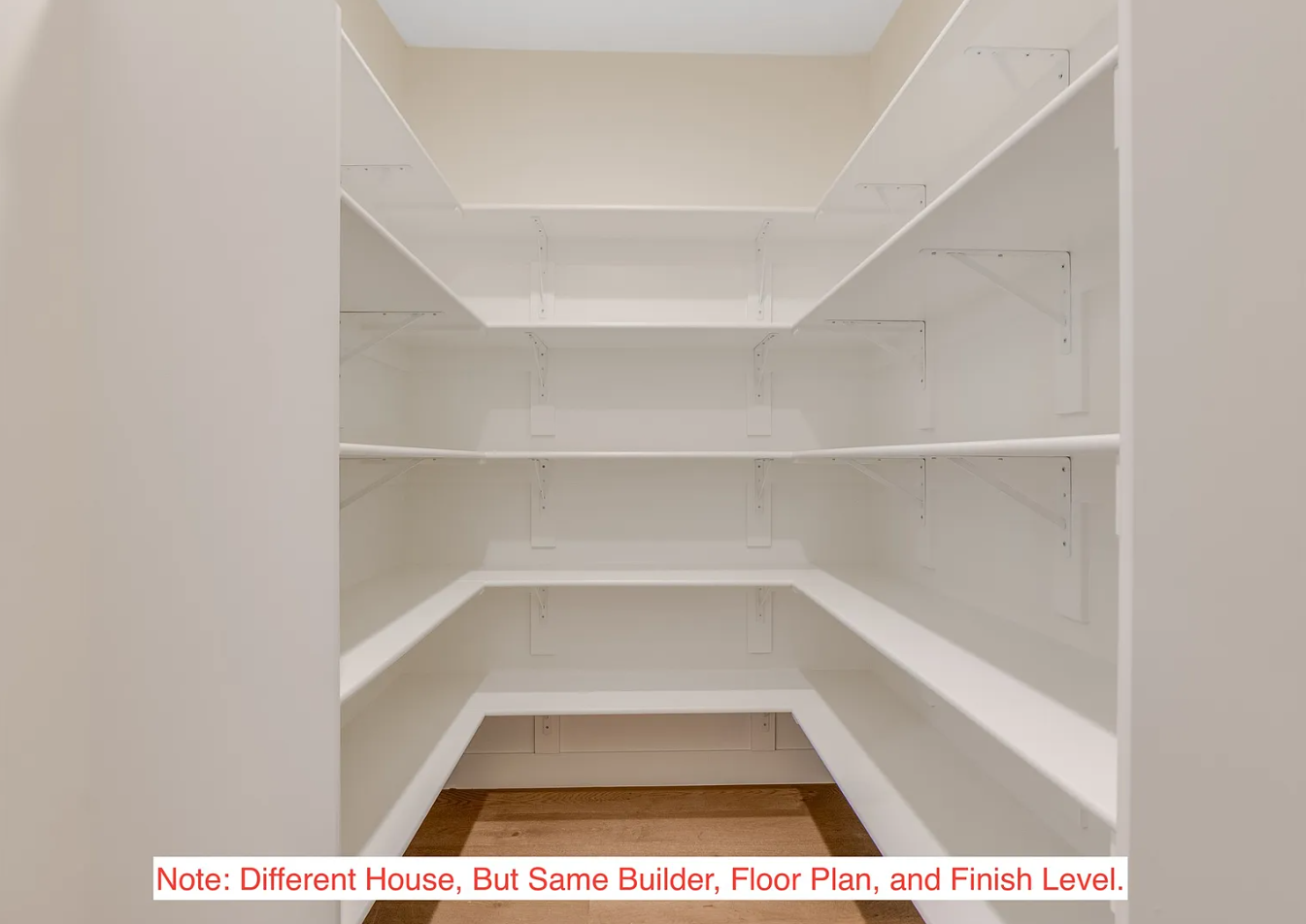 Empty white built-in corner shelving unit with four shelves inside, located in a small room with light-colored walls and a wooden floor.