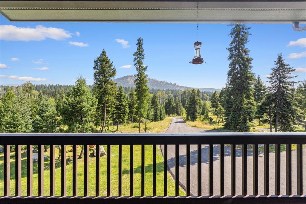 View from a balcony showing a road winding through a forest of tall evergreen trees under a partly cloudy sky.
