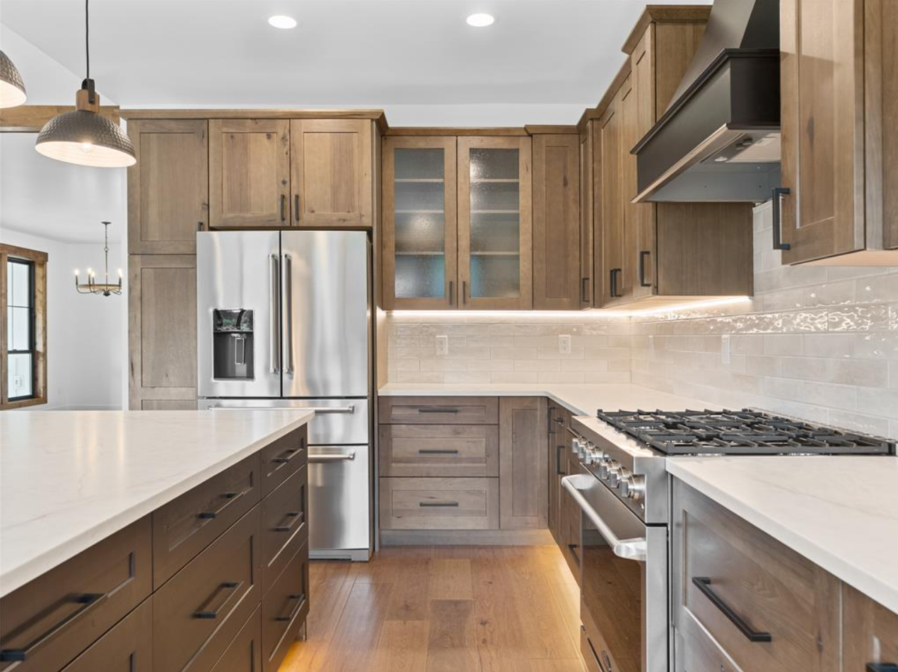 Modern kitchen with wooden cabinetry, stainless steel appliances, white countertops, and a tile backsplash.
