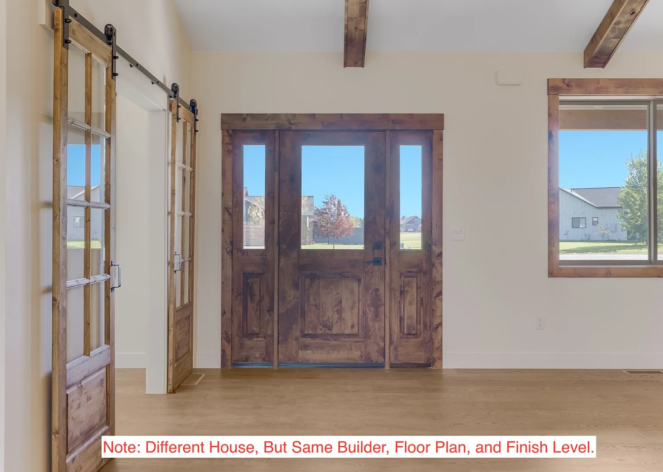 Interior view of a house entrance with wooden door and windows, light-colored walls, and hardwood flooring.