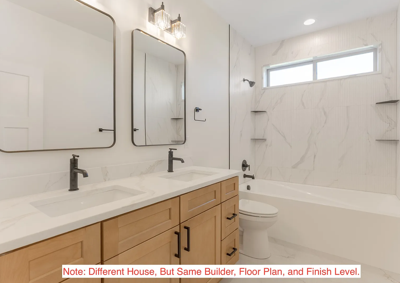 Modern bathroom with double vanity, two mirrors, and a bathtub with marble tiles, a window, and a light fixture.