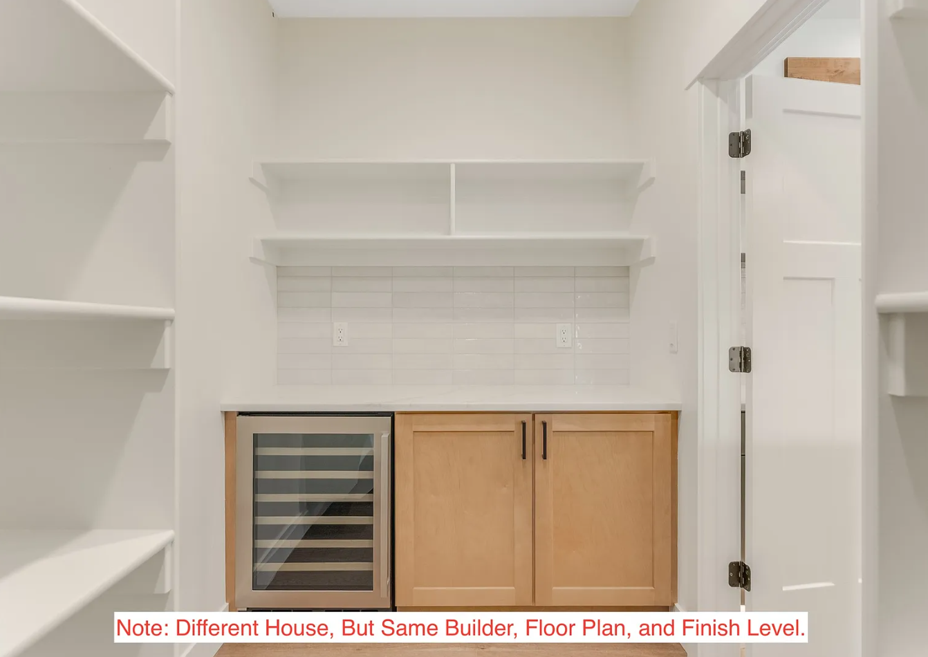 A small kitchenette with a built-in wine cooler, wooden cabinets, white shelves, white tiled backsplash, and a doorway on the right side.