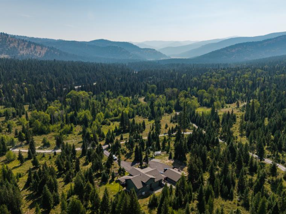 A house surrounded by dense green trees with mountains in the background and a partly cloudy sky.