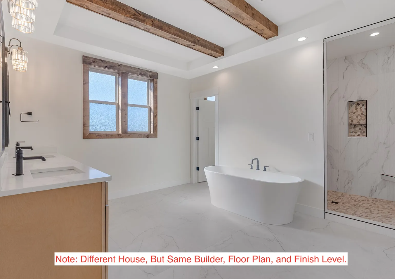 Modern bathroom with a white freestanding bathtub, double vanity with black fixtures, large window with wooden trim, marble shower with niche, and wood ceiling beams, all in a minimalistic and clean design.