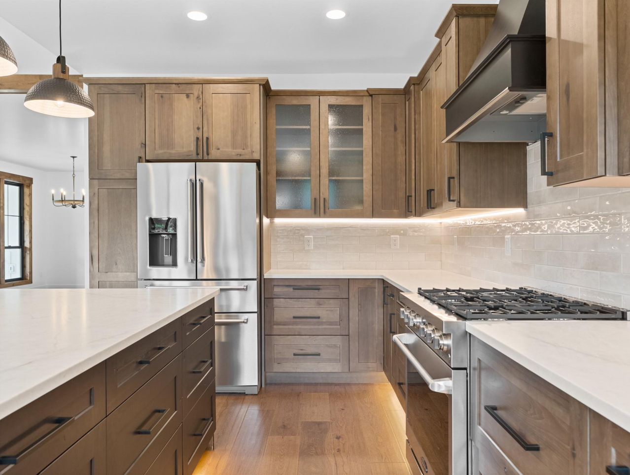 Modern kitchen with wooden cabinets, white countertops, stainless steel appliances including a refrigerator and stove, and a light-colored tile backsplash.