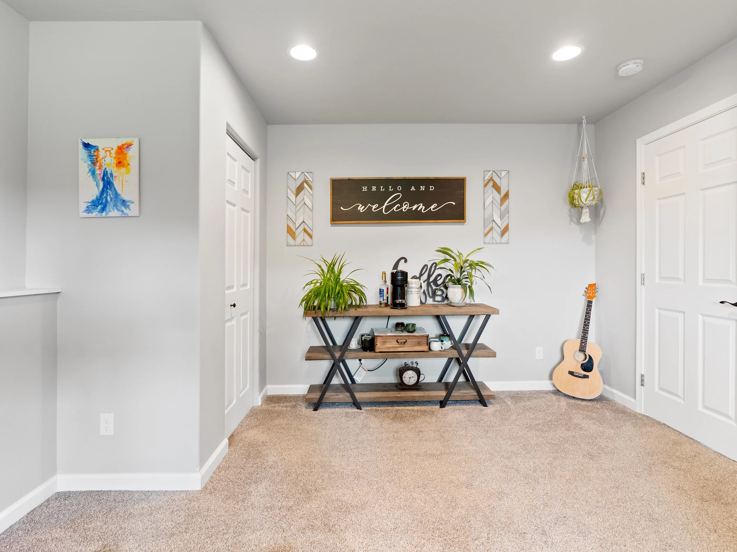 Living room with a wall decorated with a large welcome sign, framed art, plants, a coffee bar, and an acoustic guitar.
