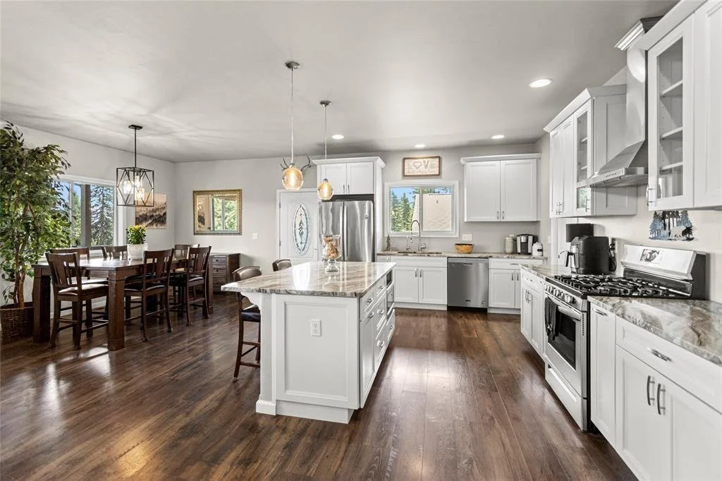 Open-concept kitchen with white cabinets, stainless steel appliances, wooden flooring, island, and dining area with wooden table and chairs.
