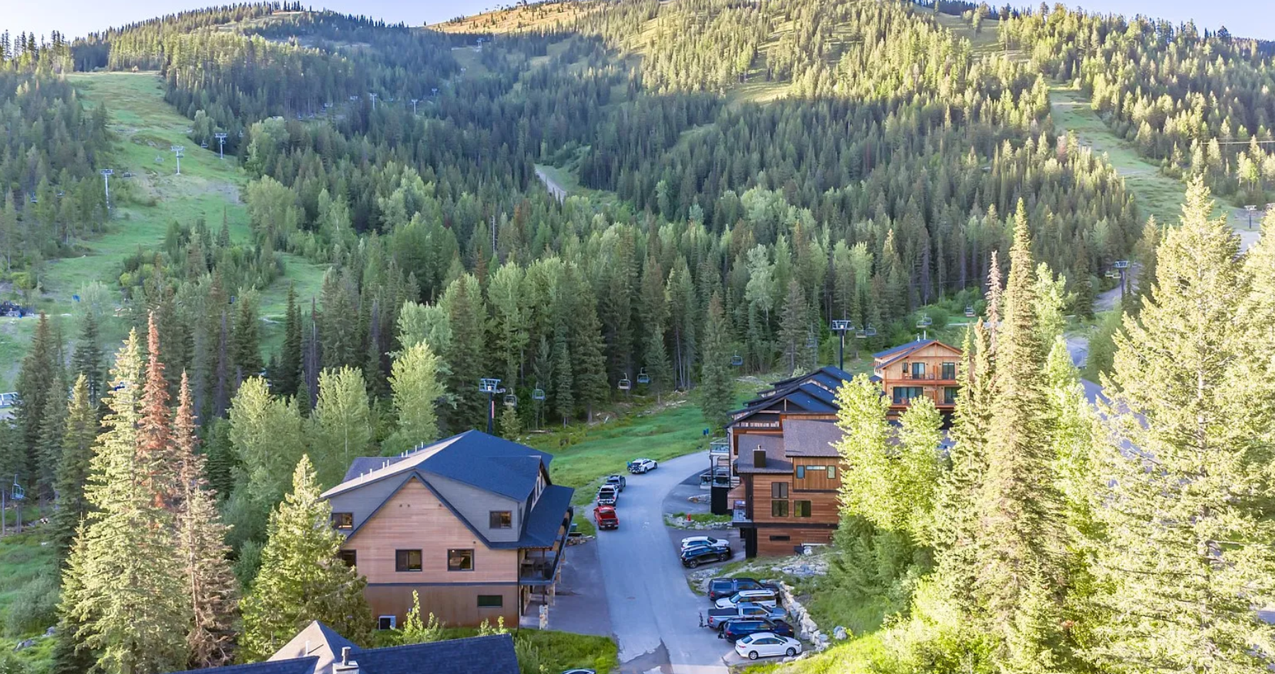 A mountain landscape with evergreen trees, ski lift chairs, and wooden buildings during daytime.