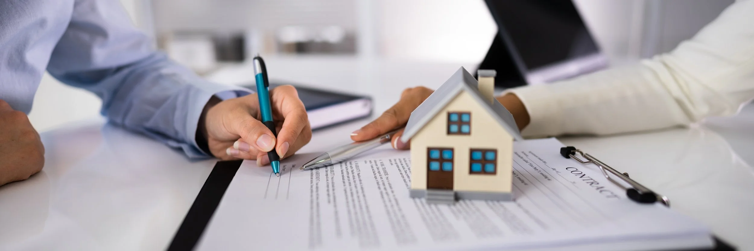 People signing a contract at a table with a small house model and documents.
