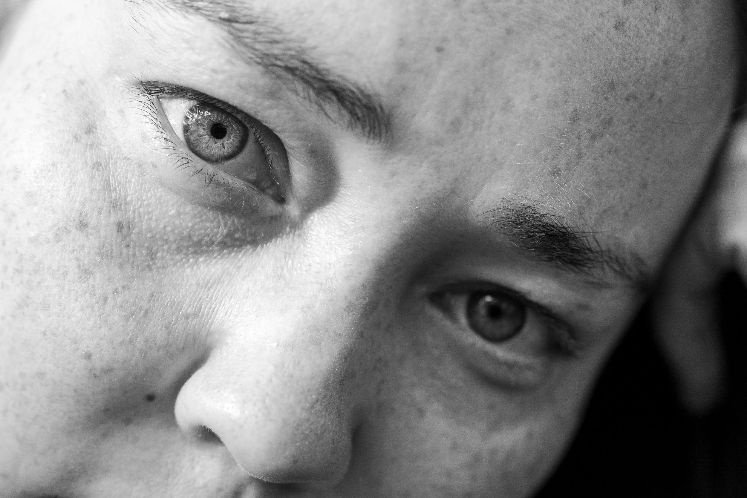 Close-up of a person's eye with detailed visibility of the iris, eyelashes, and surrounding skin in black and white.