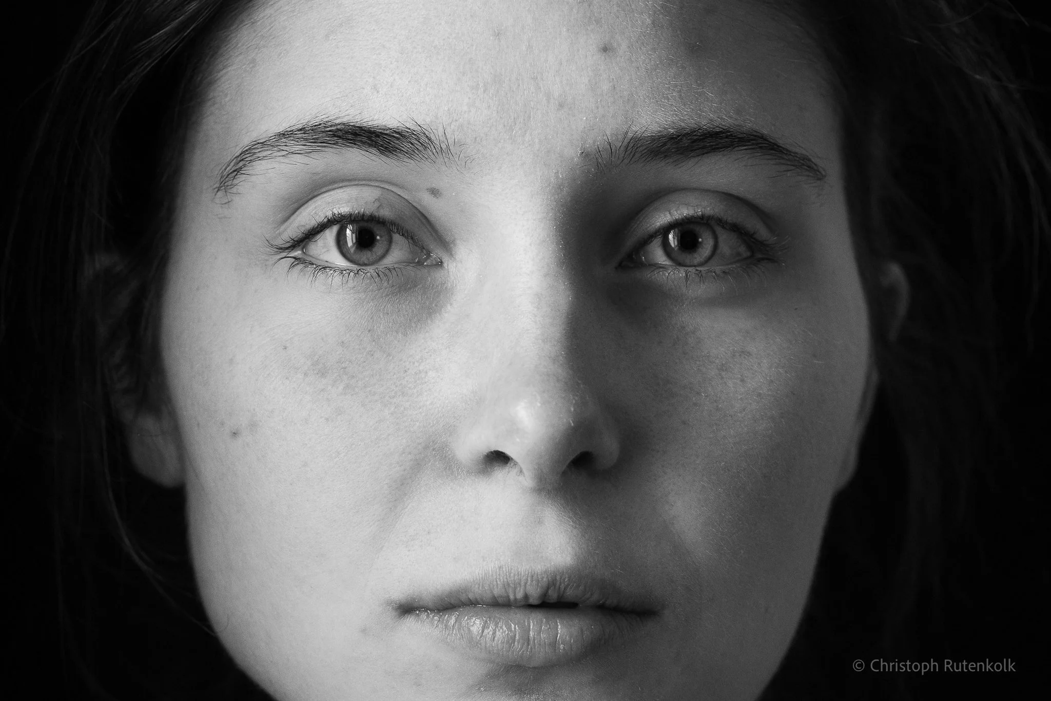 Close-up black and white photo of a woman's face, focusing on her eyes and nose with dark hair framing her face.