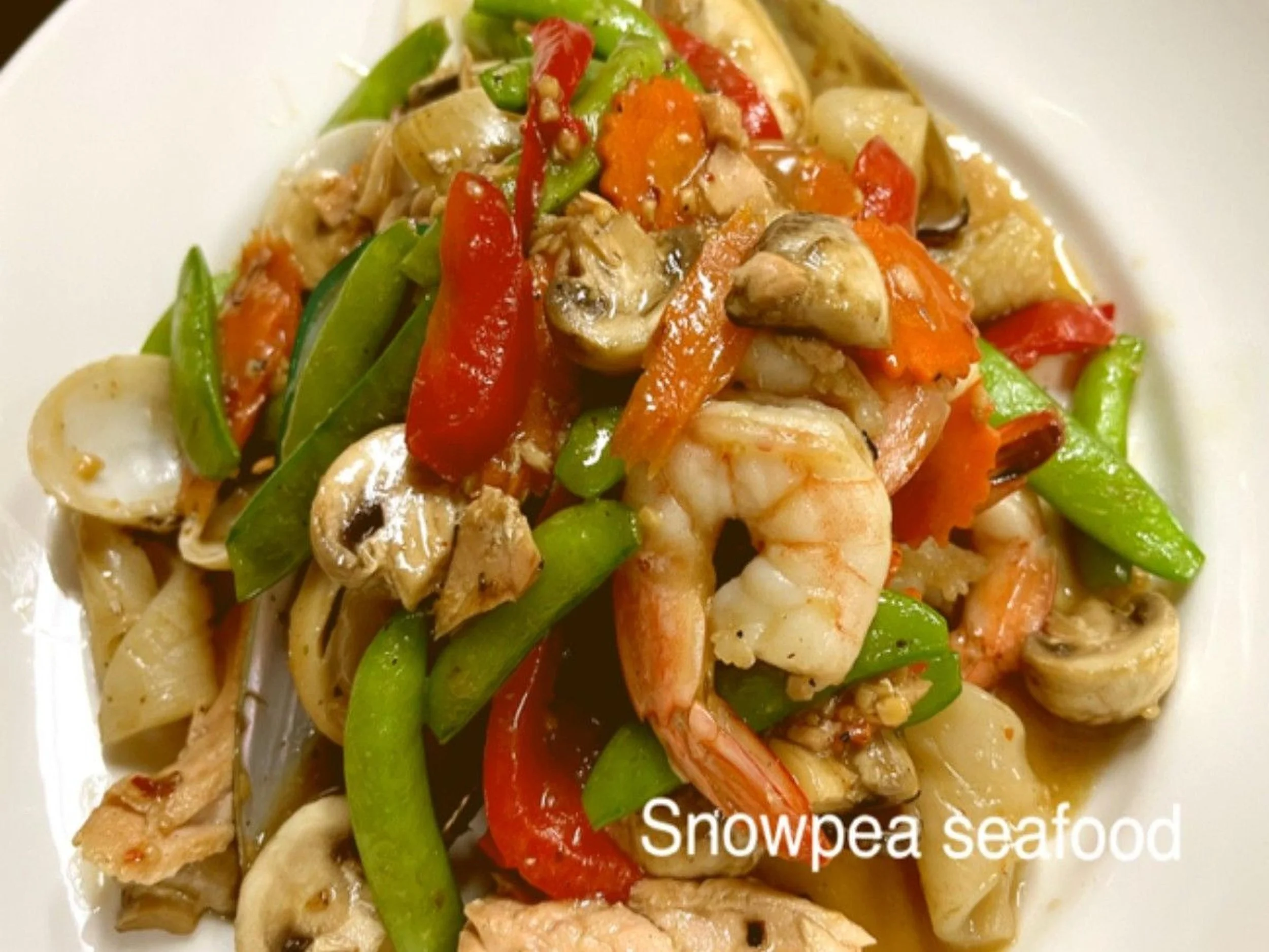 A bowl of Snowpea seafood mixture with shrimp, mushrooms, red peppers, green beans, and carrots in a savory sauce