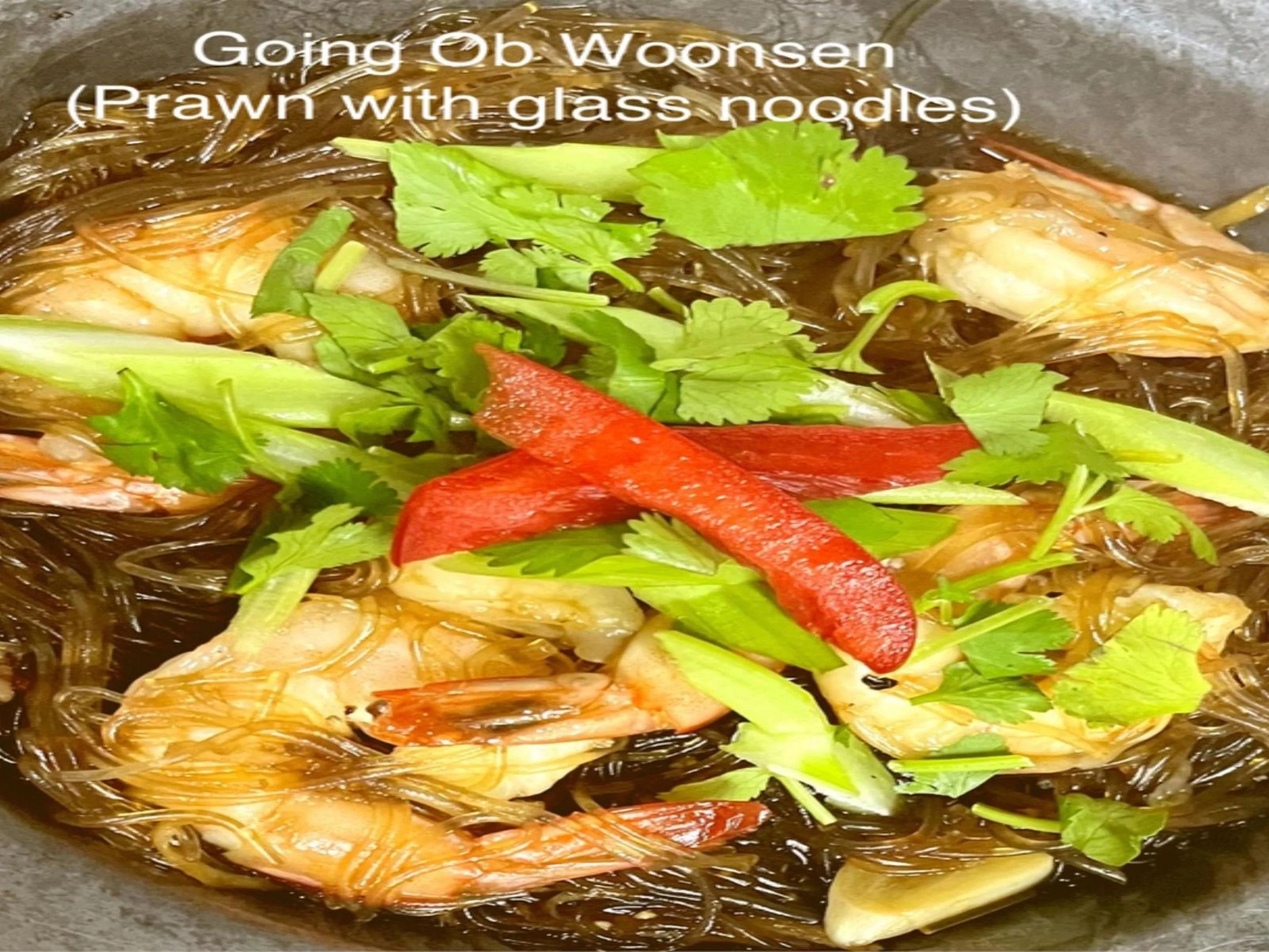 Lobster and glass noodles stir-fried with red and green bell peppers, cilantro, green onion, and garlic in a pan.