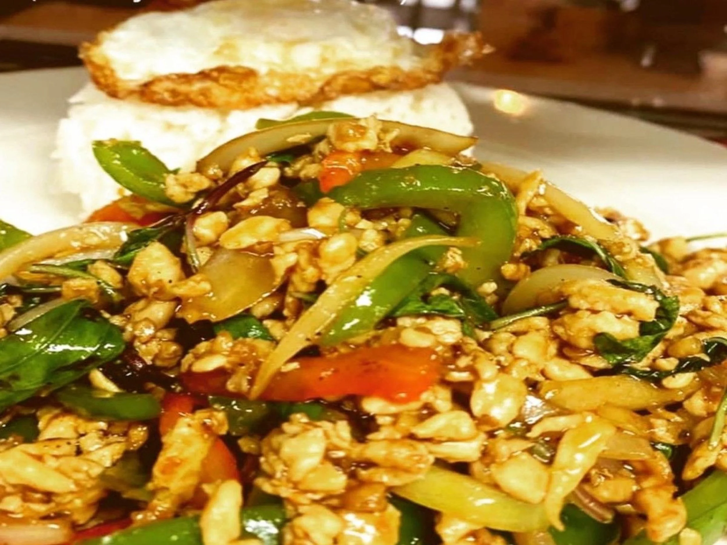 Stir-fried chicken with vegetables including green peppers, onions, and carrots, served with a scoop of rice and a fried egg on top.