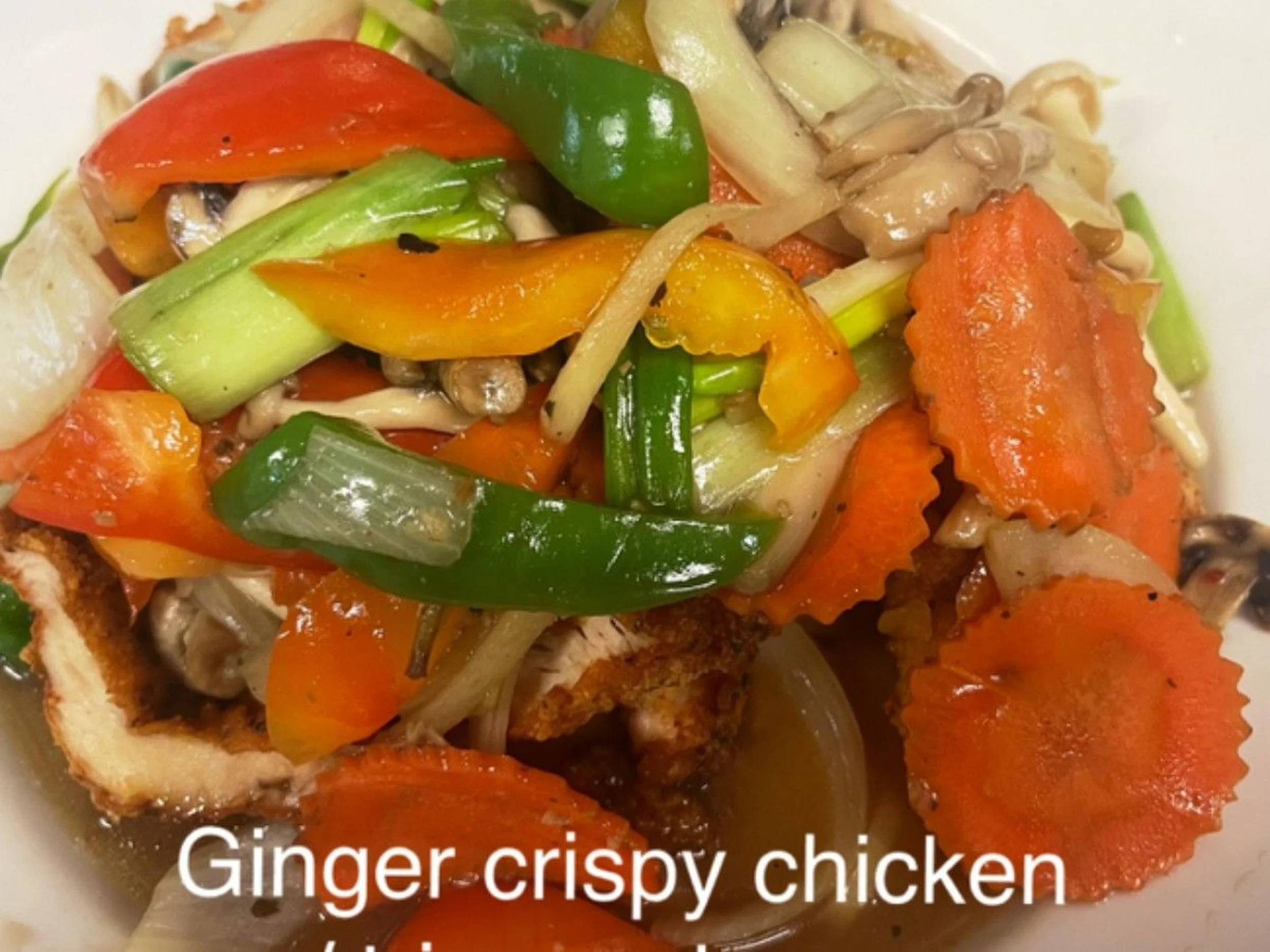 A dish of ginger crispy chicken topped with sautéed colorful vegetables including bell peppers, carrots, green onions, and mushrooms.
