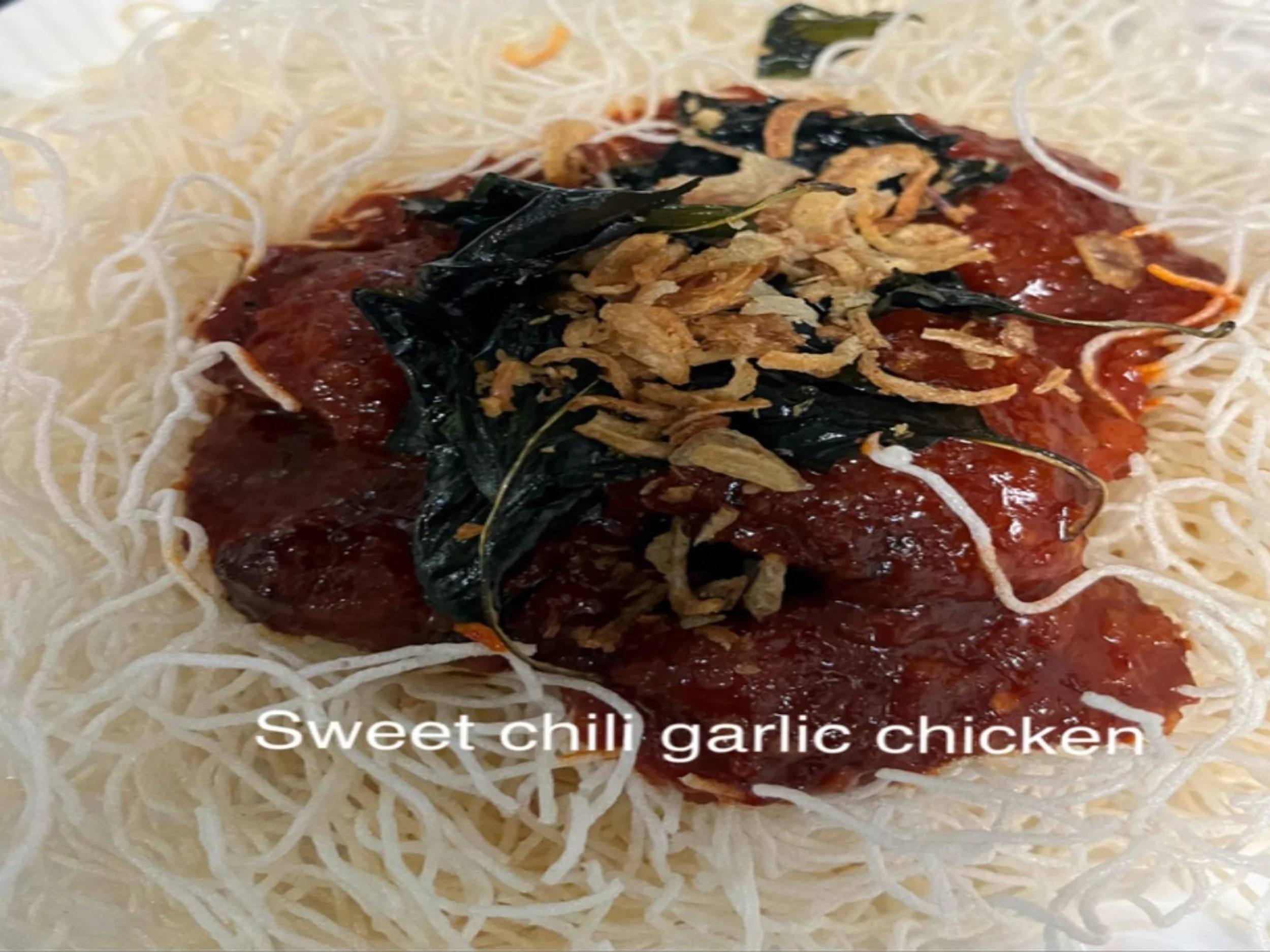 Plate of sweet chili garlic chicken served over crispy rice noodles with garnished fried shallots