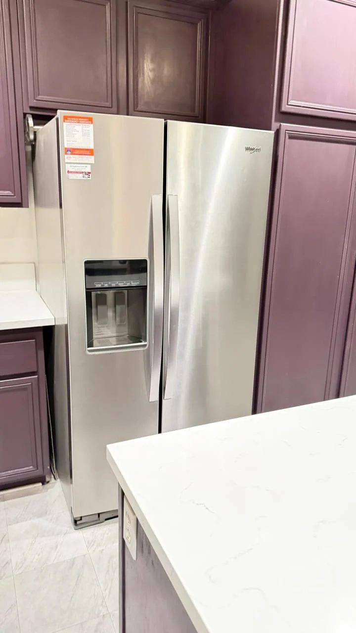 Stainless steel side-by-side refrigerator with purple kitchen cabinets and white countertop.