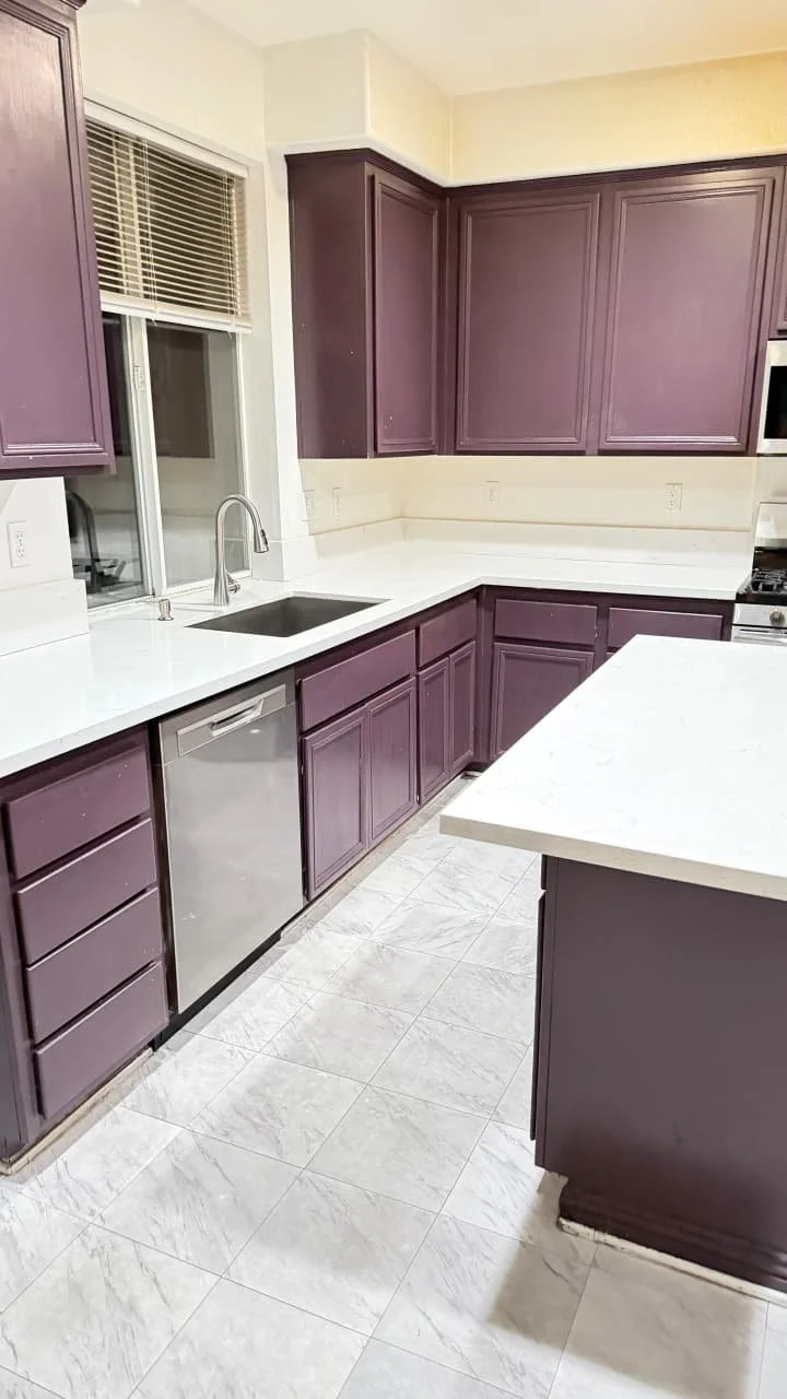 Kitchen with purple cabinets, white countertops, a stainless steel dishwasher, a window with blinds, and a white tile floor.