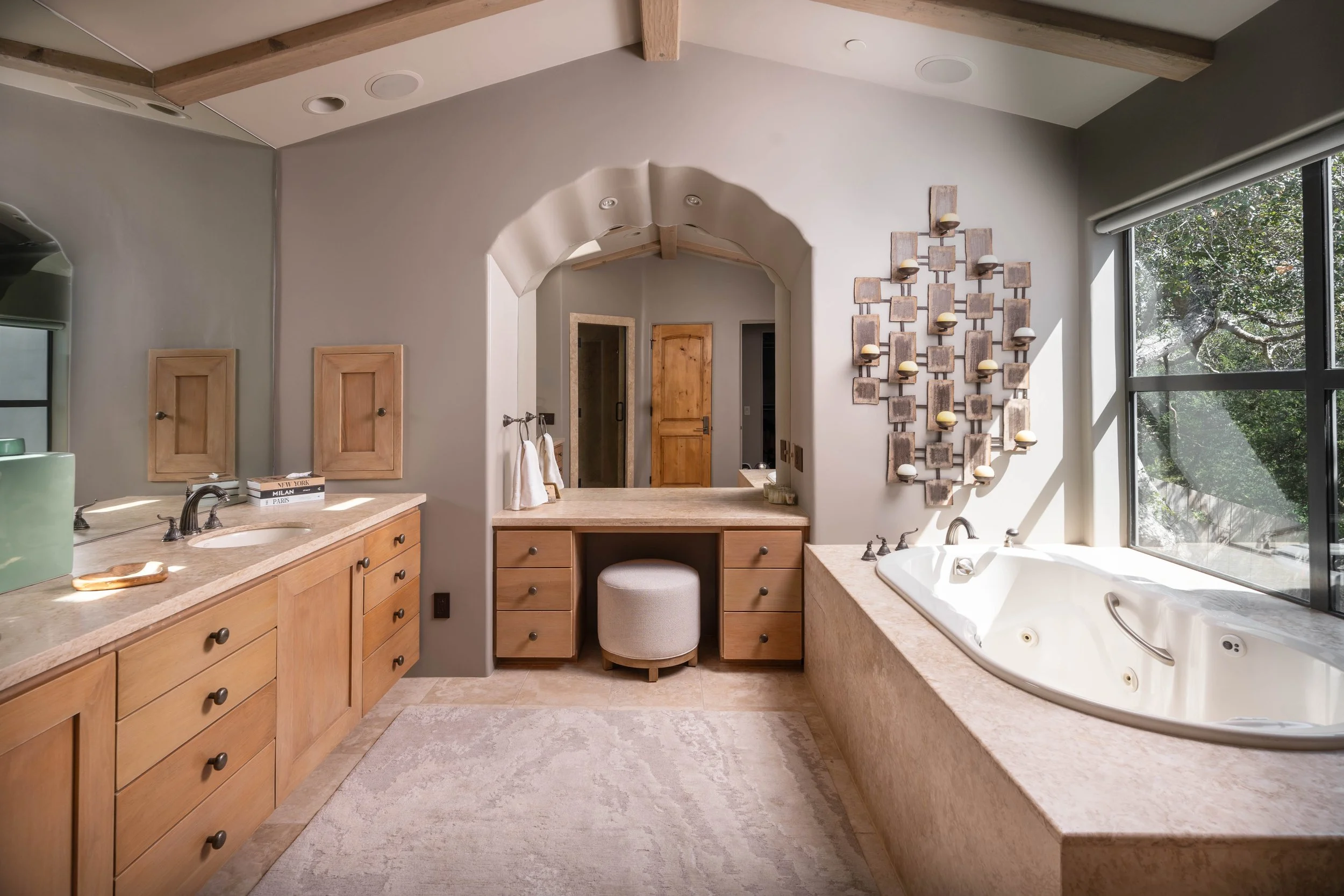 A spacious bathroom with large window, wooden cabinetry, a bathtub, and modern decor featuring wall-mounted candle holders.