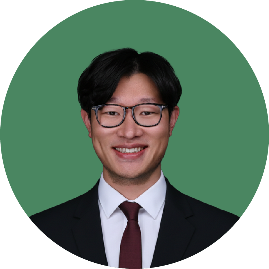 A smiling man with black hair and glasses, dressed in a suit and tie, against a green background.