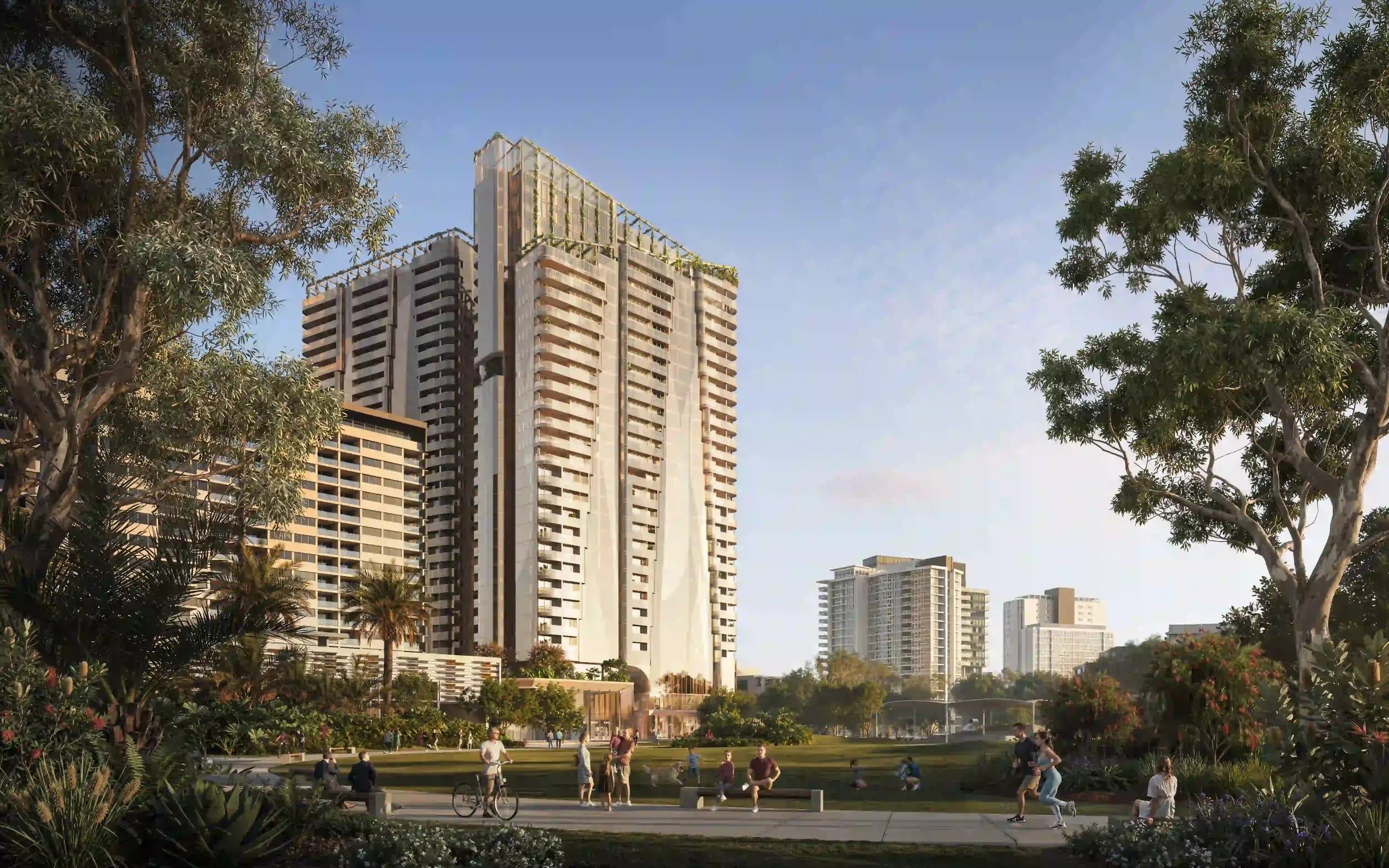 People enjoying a park with tall buildings in the background, trees surrounding the scene, some individuals are walking, cycling, and sitting on benches, under a clear sky.