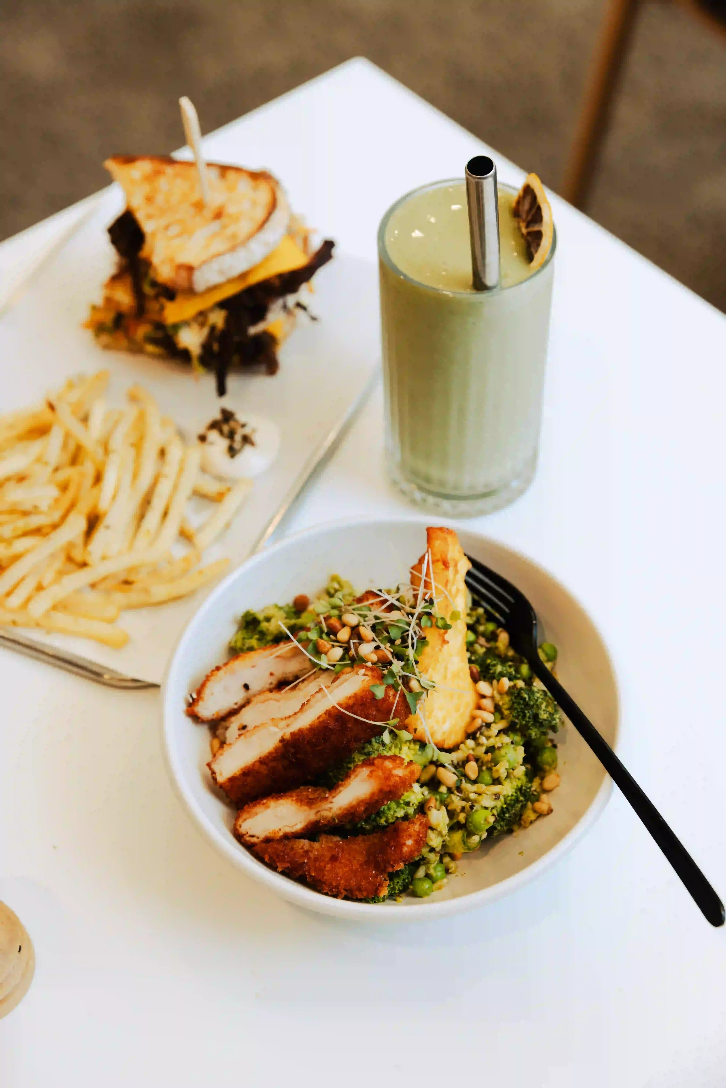 A white bowl filled with chopped grilled chicken, broccoli, and topped with microgreens and pine nuts.