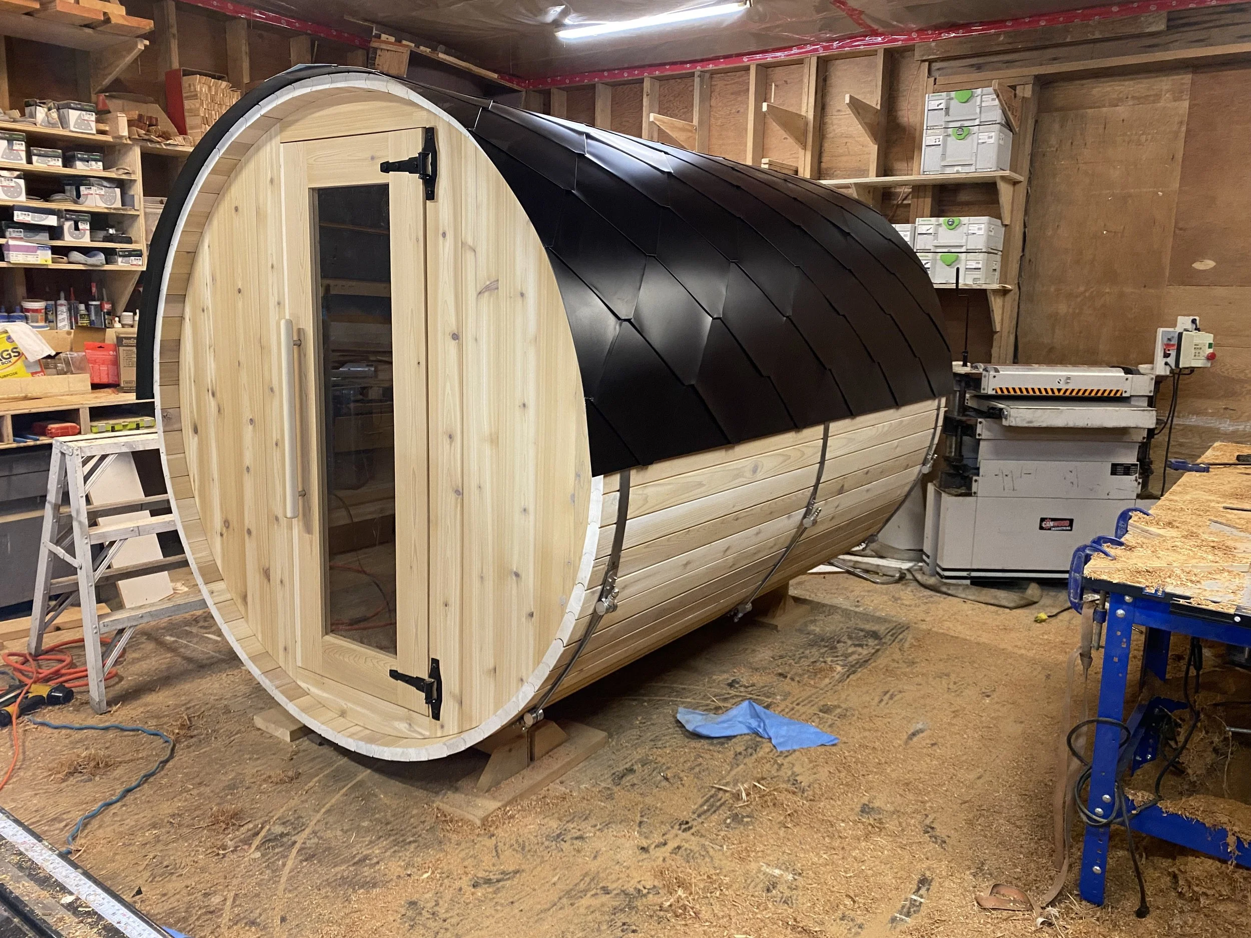 Classic cedar barrel sauna with a natural finish, glass door, and black aluminum roof.