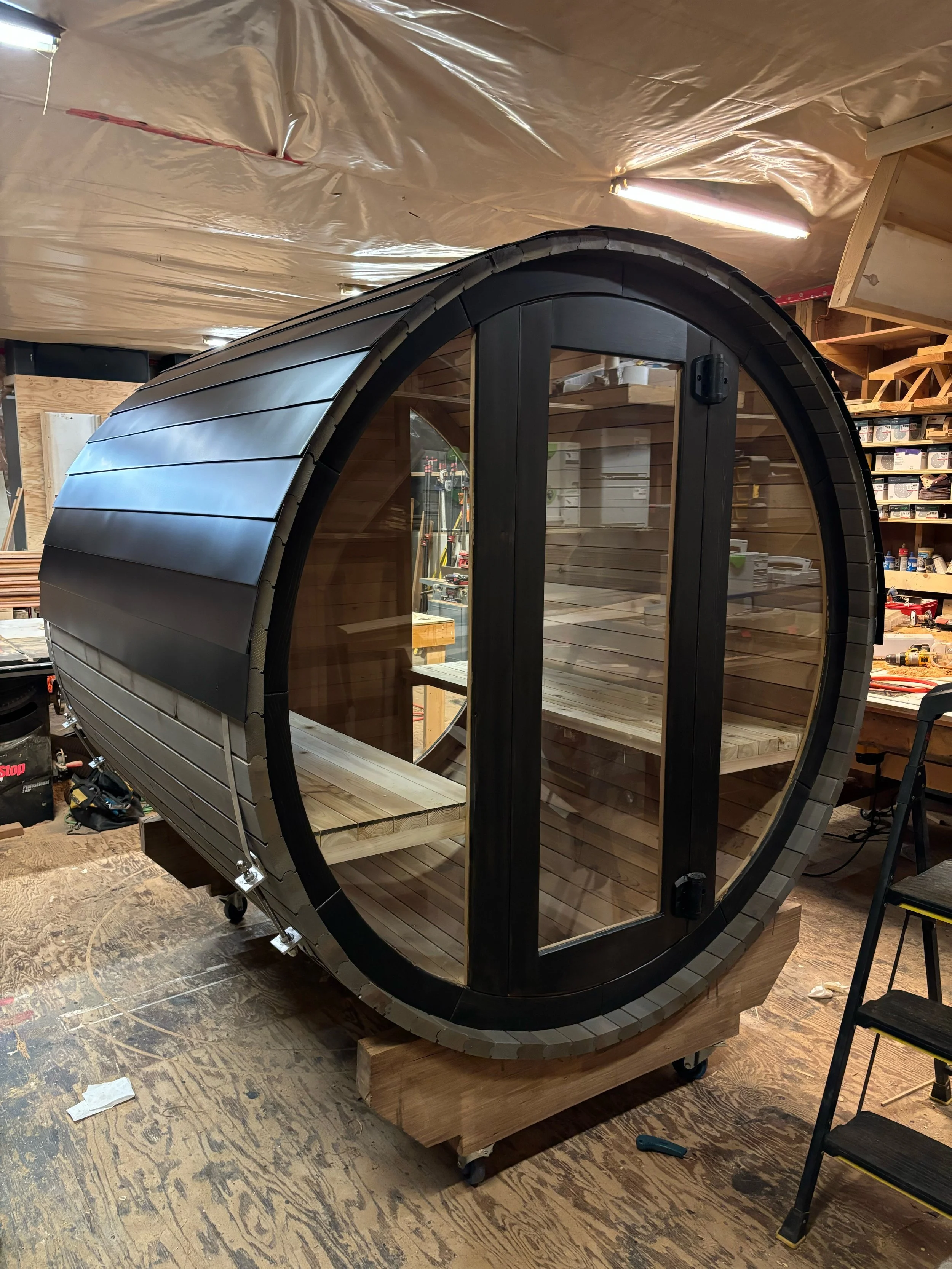 Cedar barrel sauna with a sleek dark finish, full glass door, and handcrafted aluminum roof.