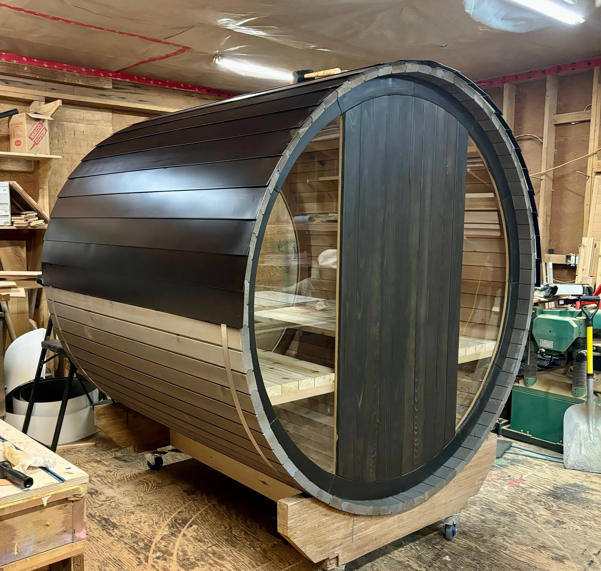 Cedar barrel sauna with a sleek dark finish, rear glass panels, and handcrafted aluminum roof.