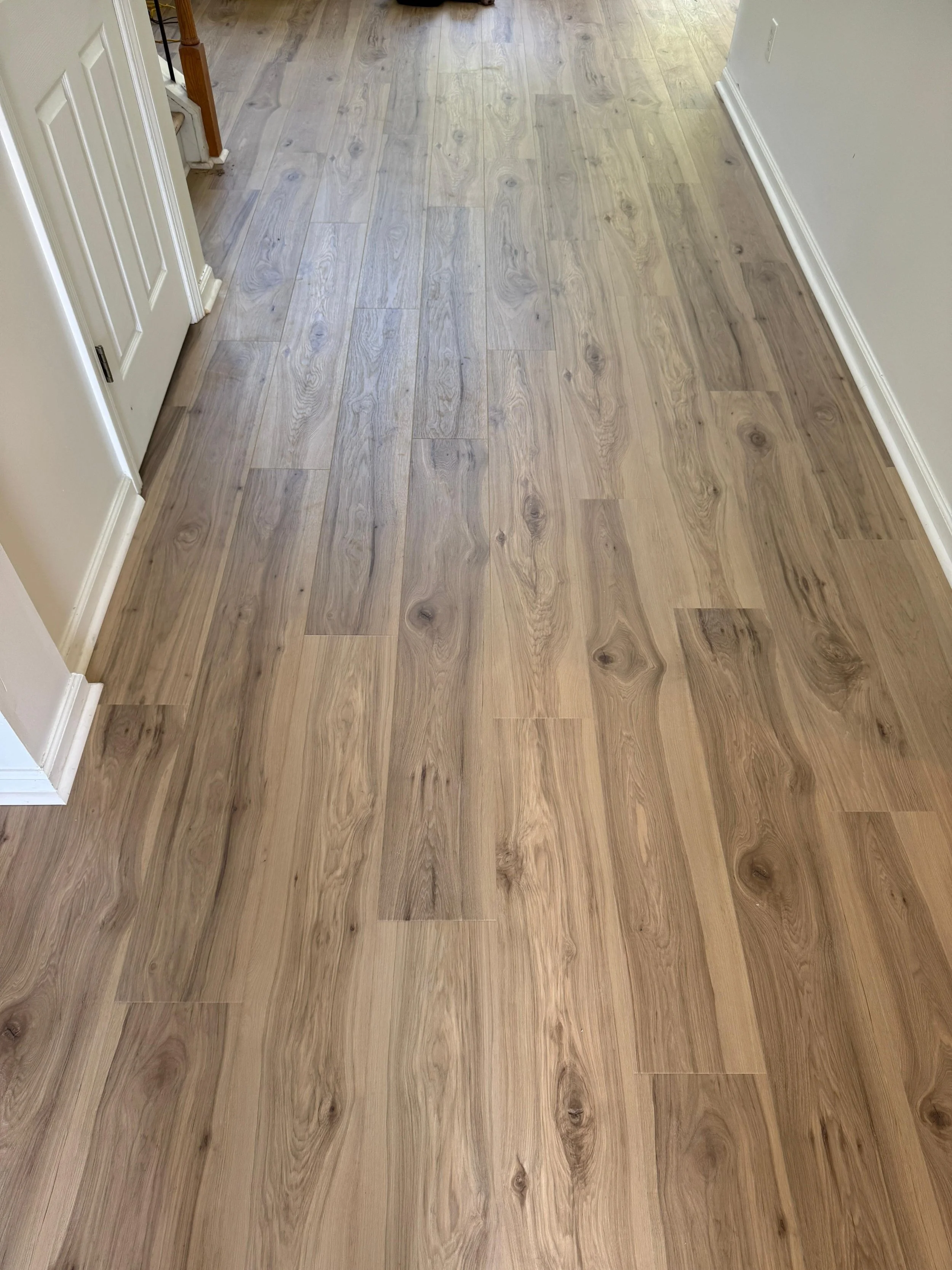 hardwood floors in a room with white walls, baseboards, and part of a door visible on the left side of the image.