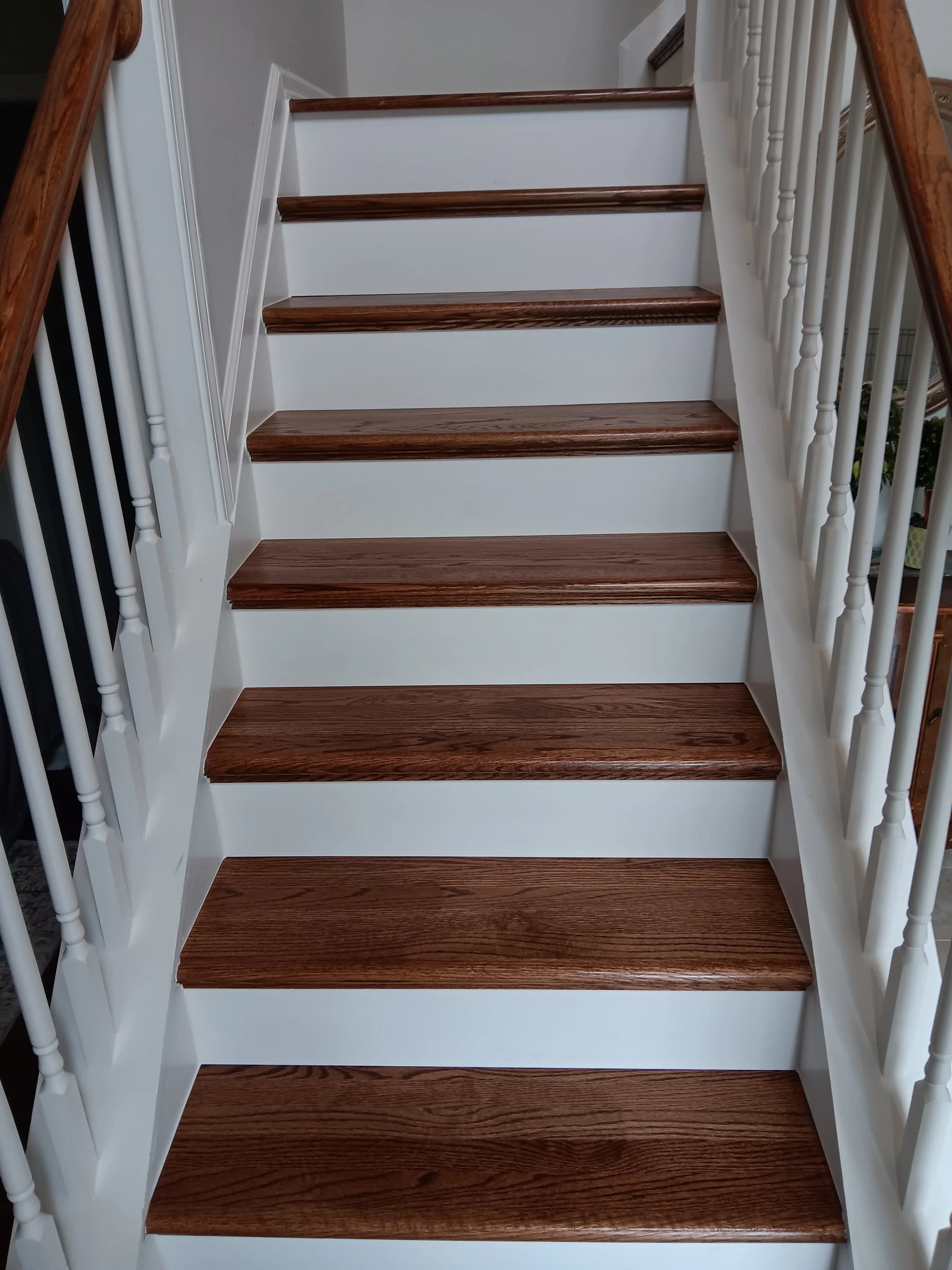 Indoor staircase with wooden steps, white risers, and white and wood handrails.