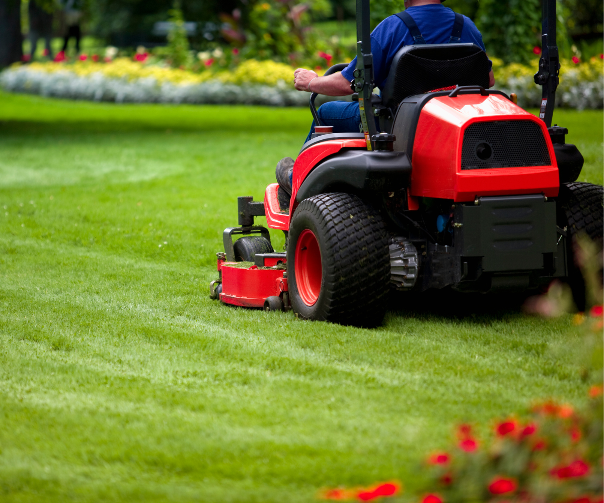 A person riding a red riding mower on a well-maintained green lawn in a garden.