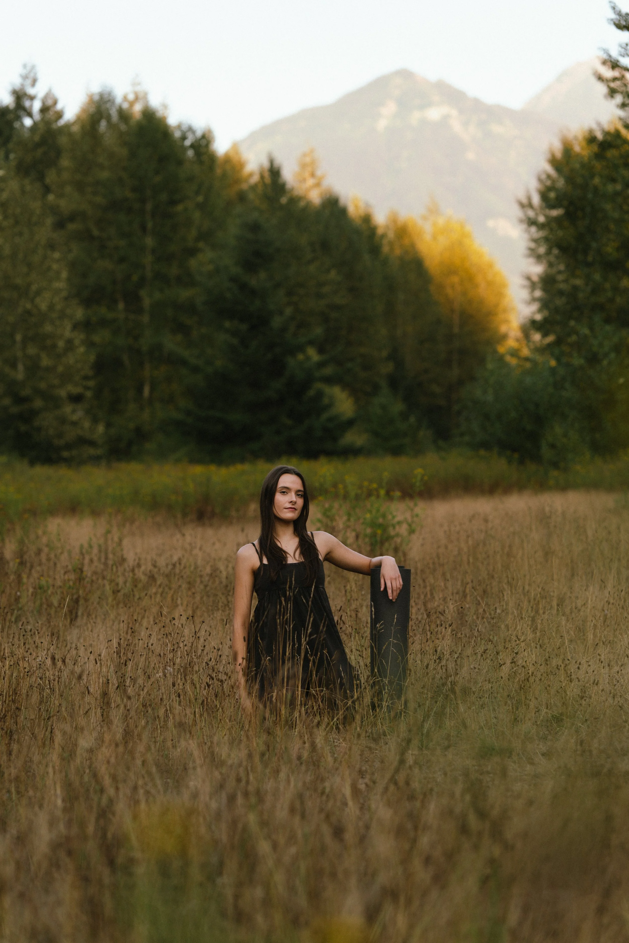 Shaina standing in a meadow with her arm against her yoga mat.