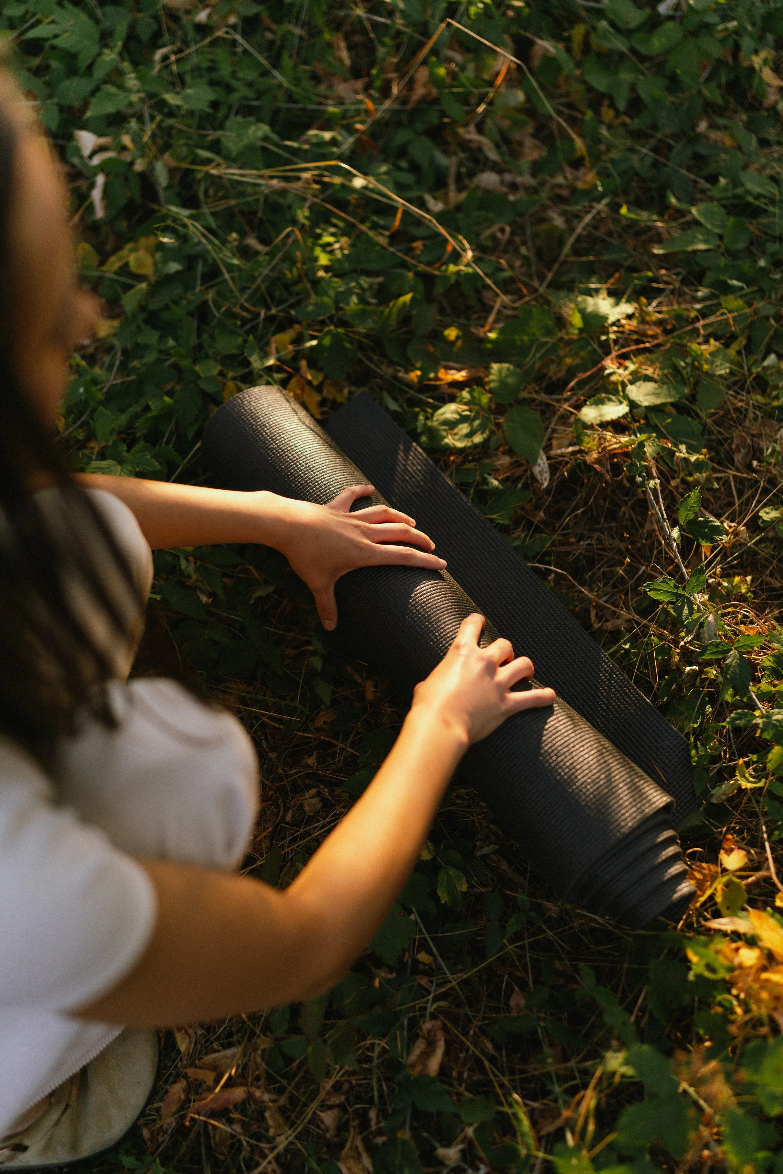 Shaina rolling up her yoga mat after teaching a yoga class, she is wearing white and outside in a meadow.
