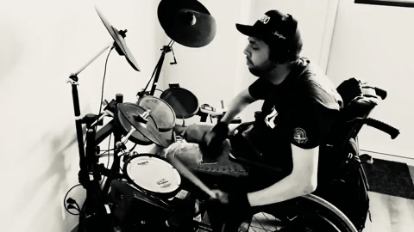 A person in a wheelchair playing electronic drums in a room.