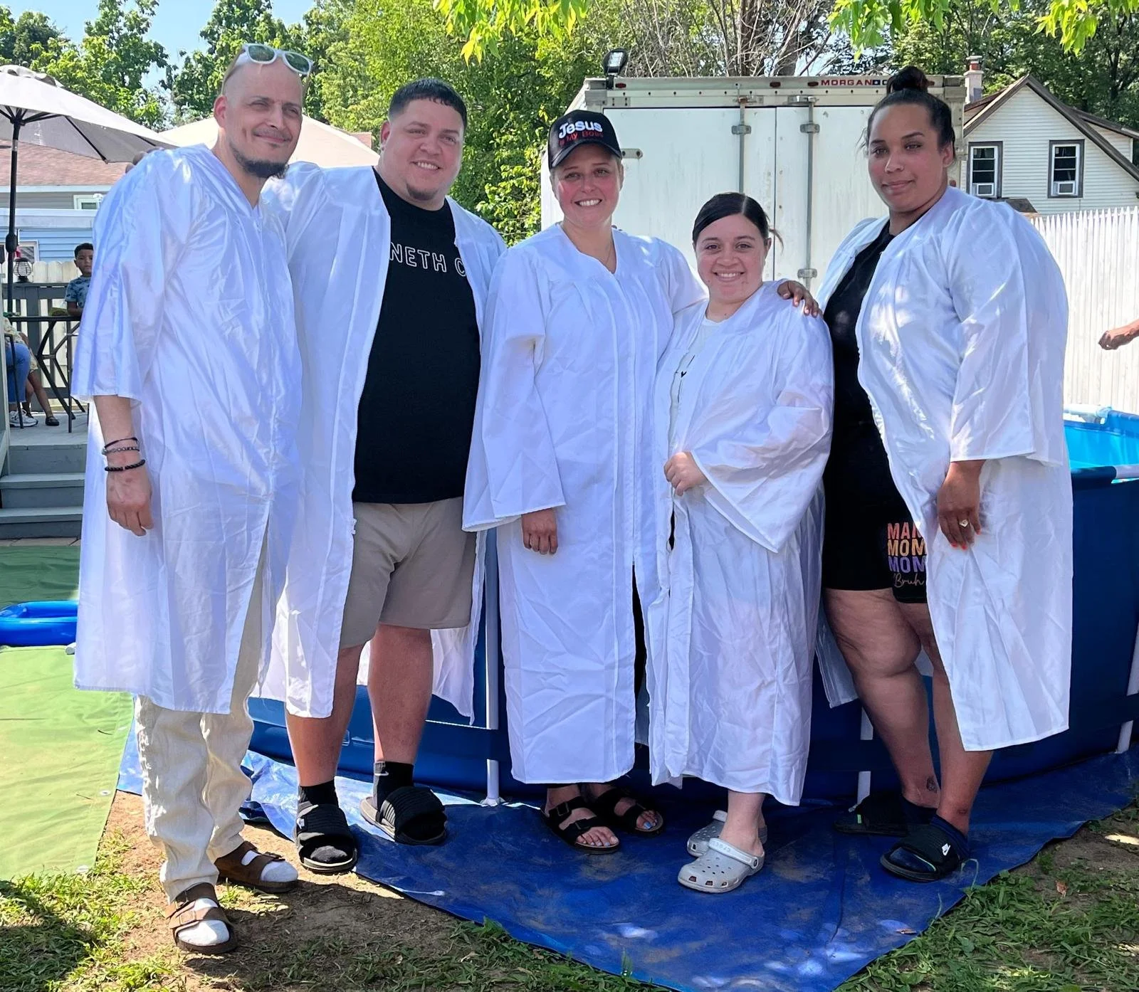 Group of six people outdoors, wearing white robes, with some smiling and posing for the photo.