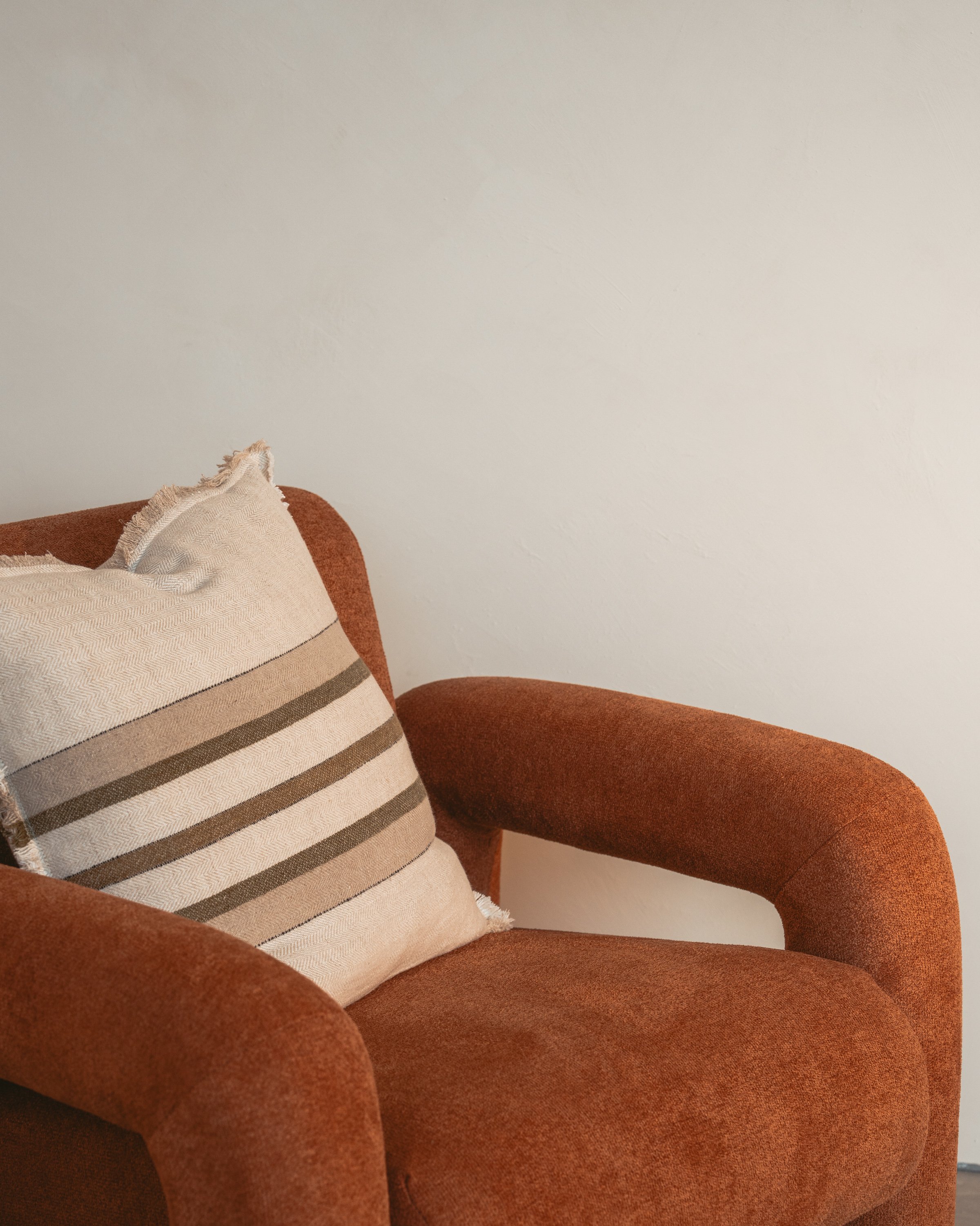 Close up of a burnt orange feature chair with a neutral striped cushion