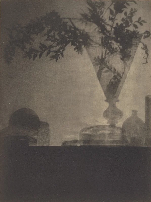 Silhouette of a vase with flowers and other containers on a surface, as seen in a shadow or silhouette.