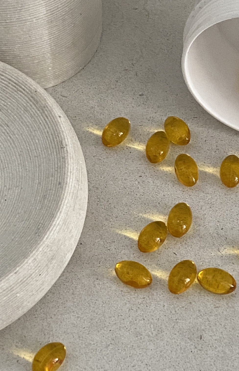 Yellow softgel capsules scattered on a light-colored surface near white ceramic dishware.