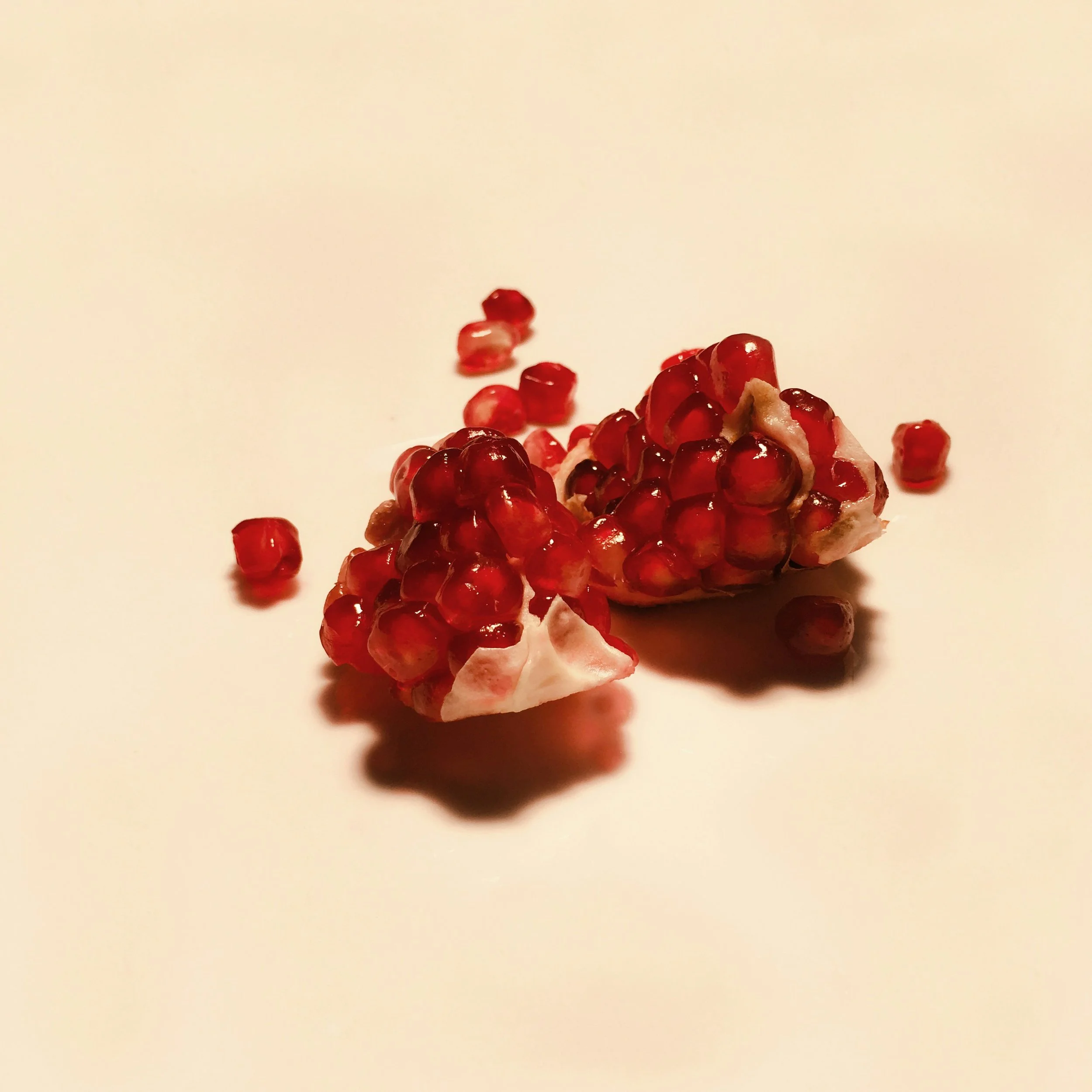 A broken pomegranate with red seeds scattered on a white surface.