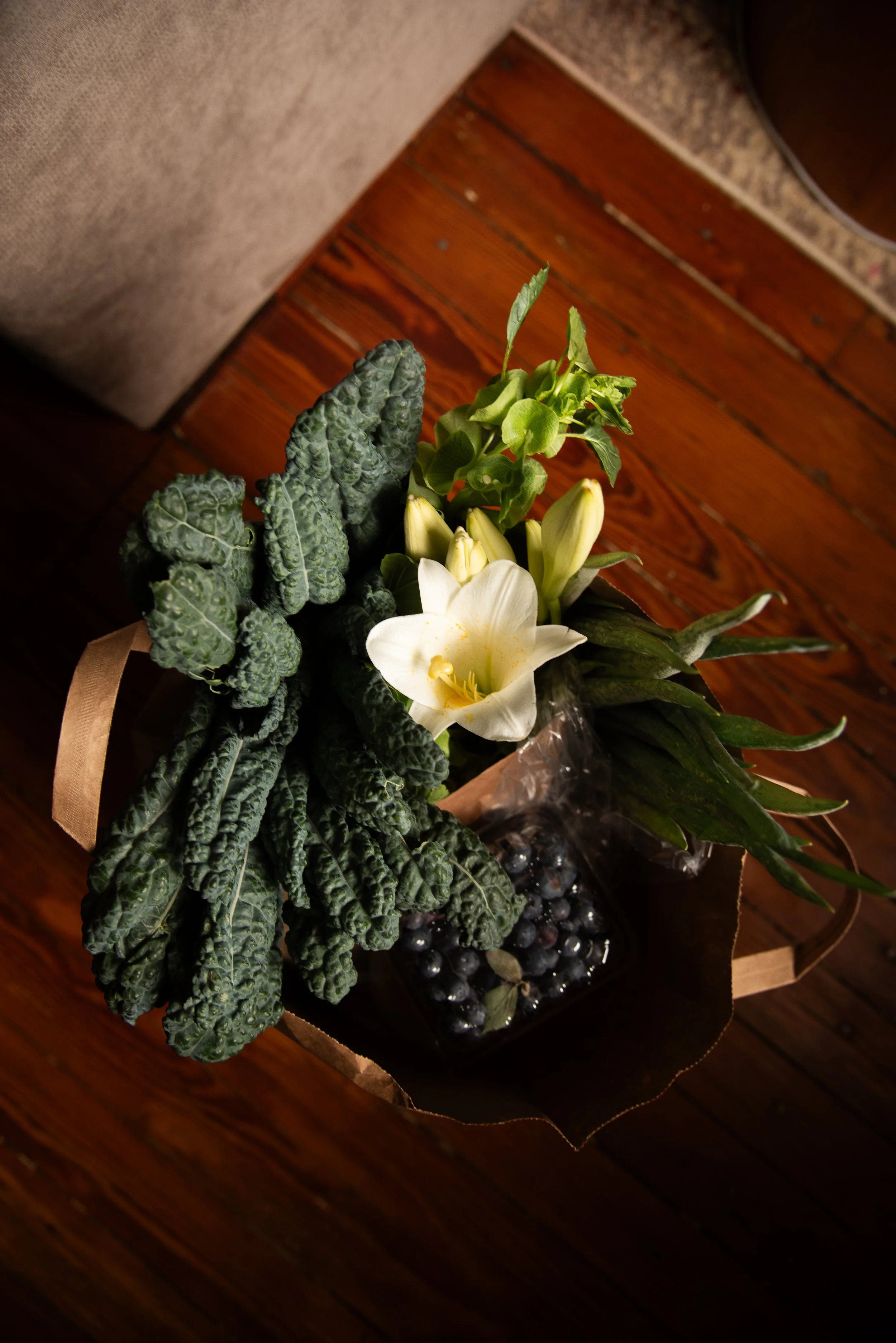 A bouquet of white lilies, green leaves, and dark purple berries on a wooden surface.