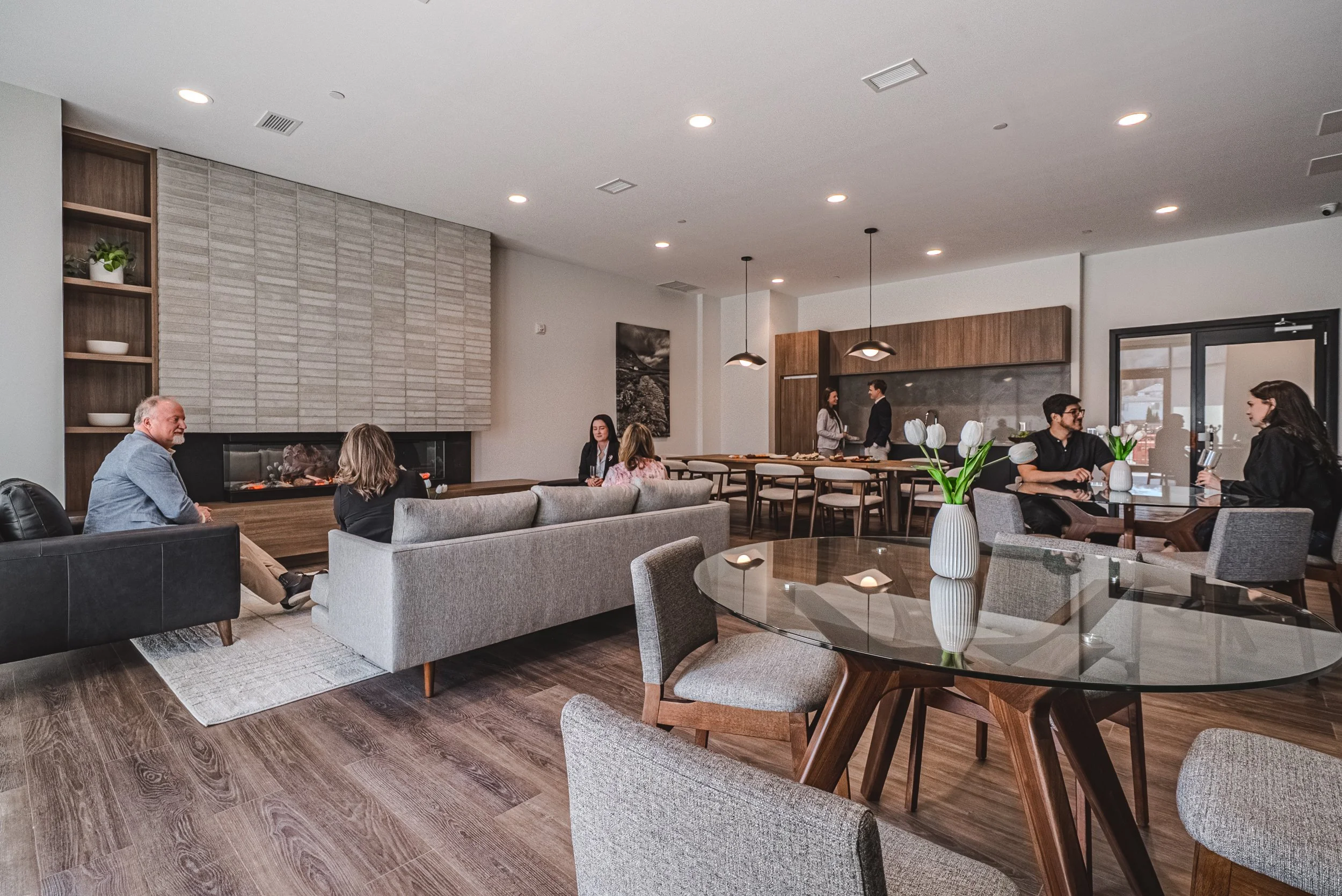Modern living room with people sitting and talking, wooden and fabric furniture, candles, and a minimalist fireplace.