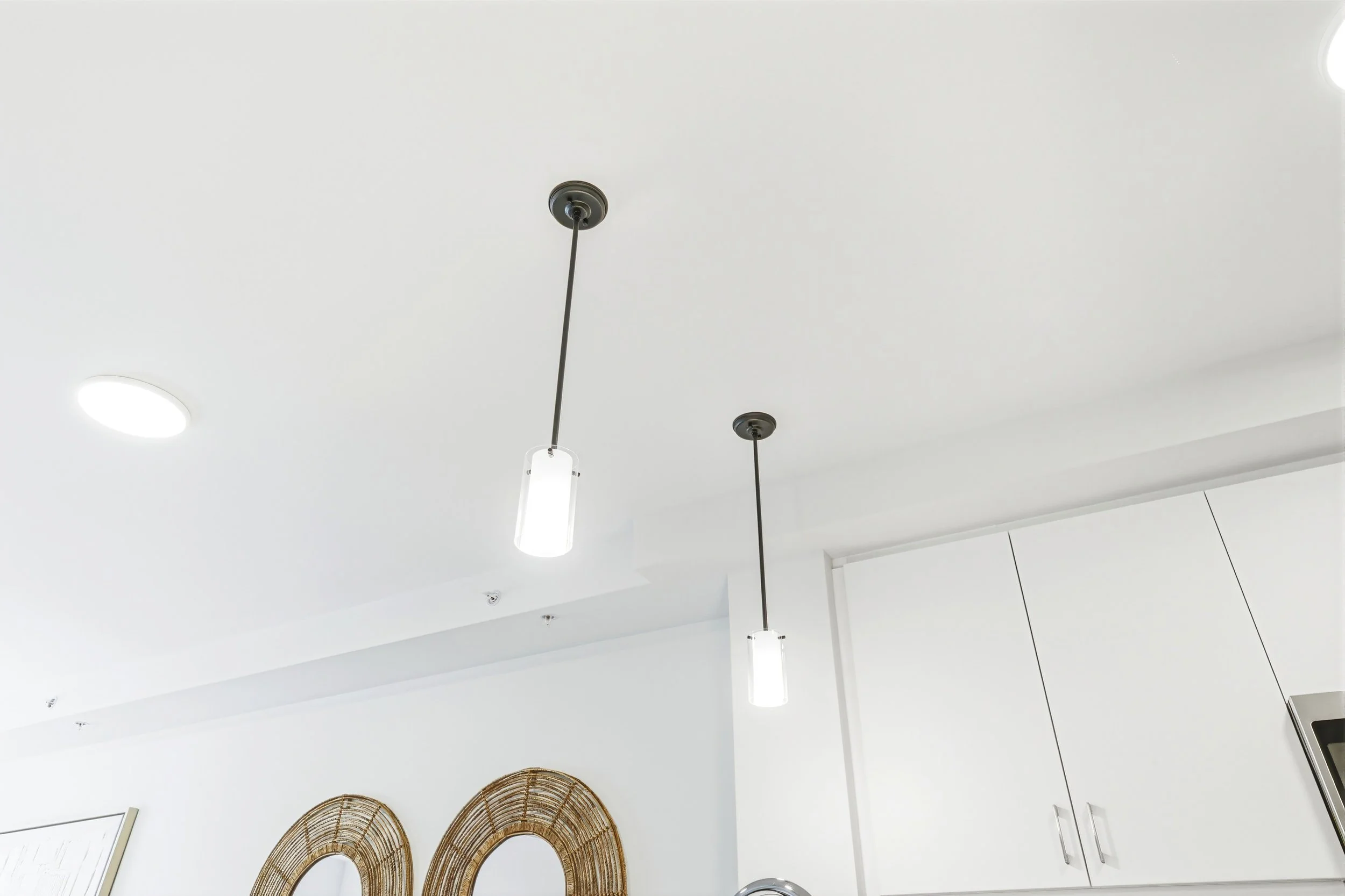 Modern kitchen ceiling with two pendant lights, recessed lighting, and white cabinets.