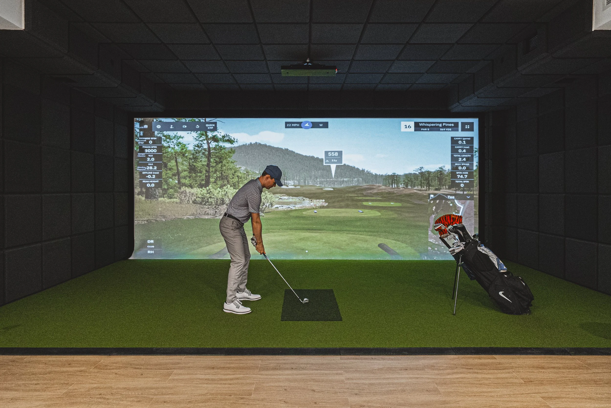 Man practicing golf indoors on a simulator with a large screen displaying a golf course scene.