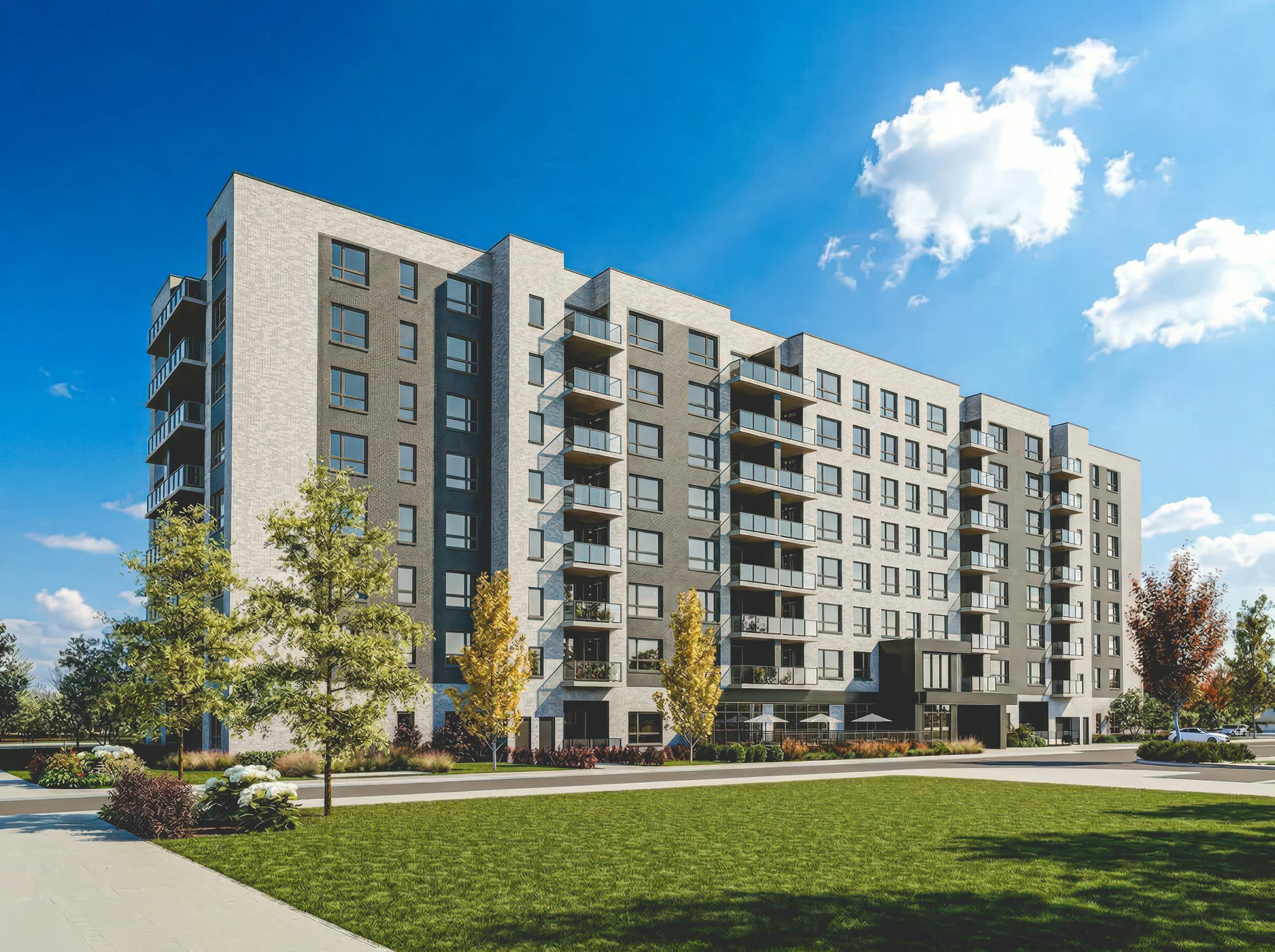 A modern multi-story apartment building with balconies, surrounded by landscaped greenery and trees, under a bright blue sky with some clouds.