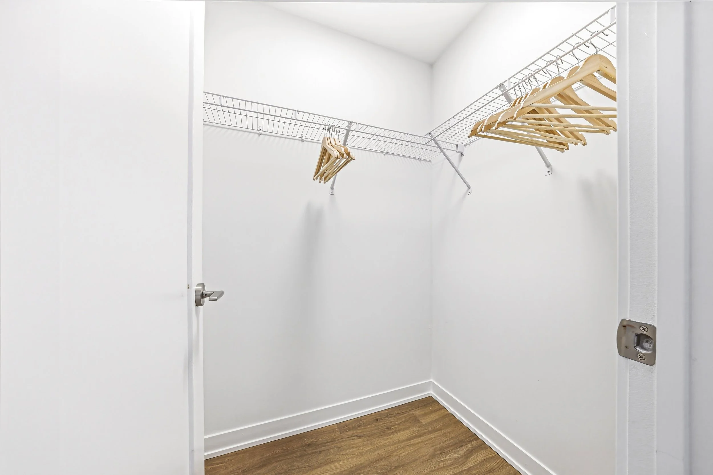 Empty walk-in closet with white walls, wooden floor, and metal wire shelving with wooden hangers.