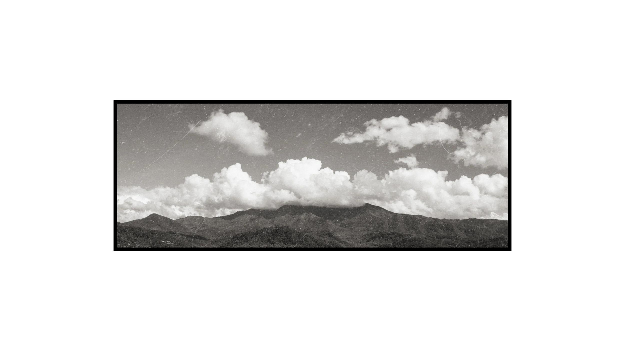 Black and white landscape photograph of mountains under a partly cloudy sky.