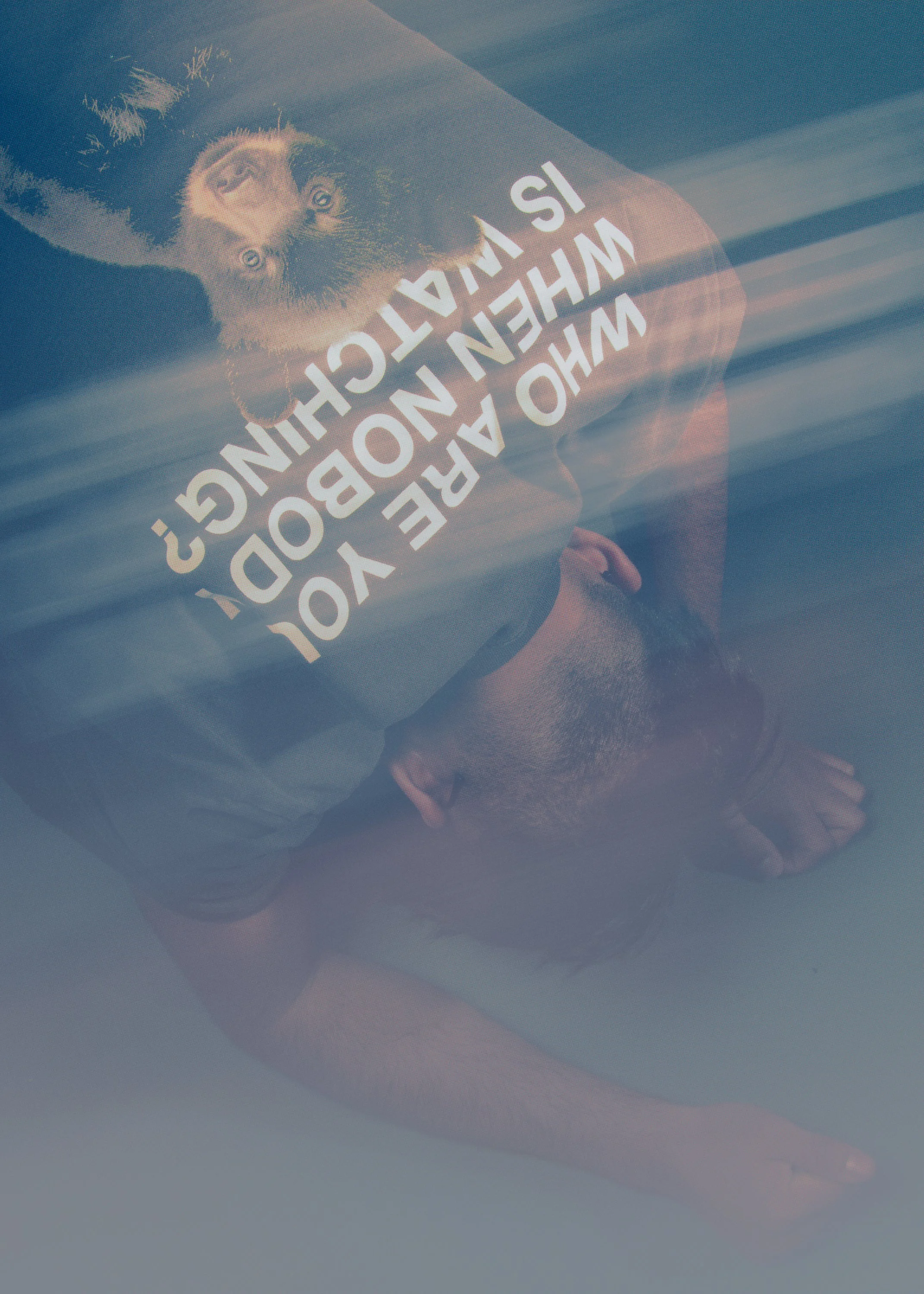 A man lying on the ground with his arm extended and head resting on his arm, wearing a t-shirt with a dog print and text in Spanish, and a reflection of a tree or light streaks above him.