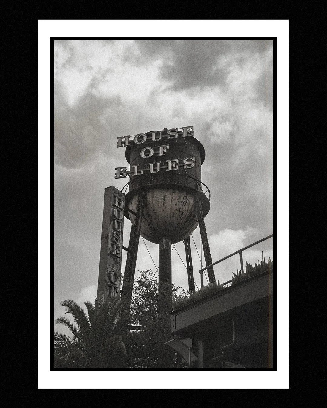 Old water tower with neon signs reading 'HOUSE OF BLUES' in a cloudy sky, black and white photo.