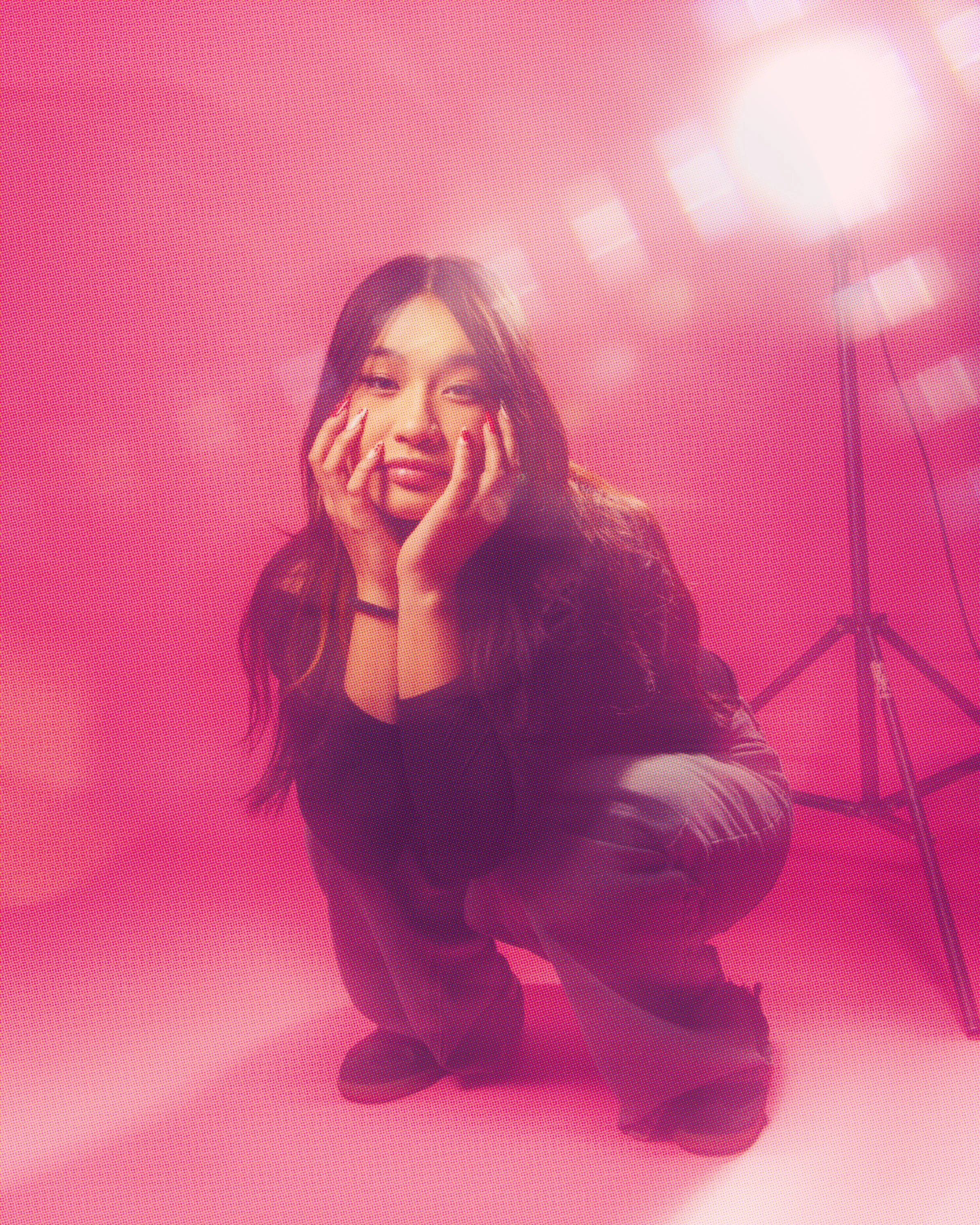 A woman with long hair posing against a pink background with bright lights.